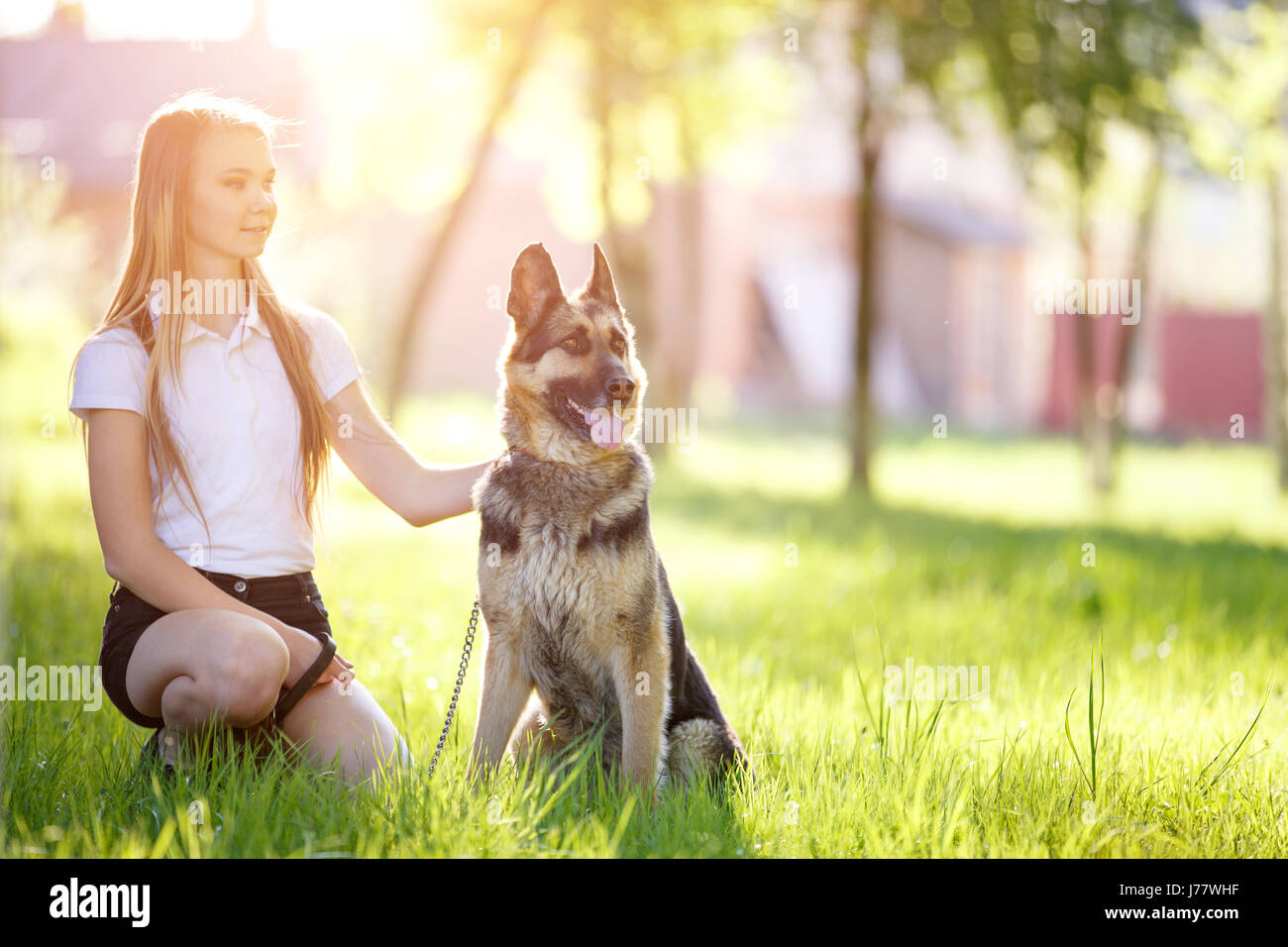 Teenage girl in white shirt with her dog sitting on grass in the park ...