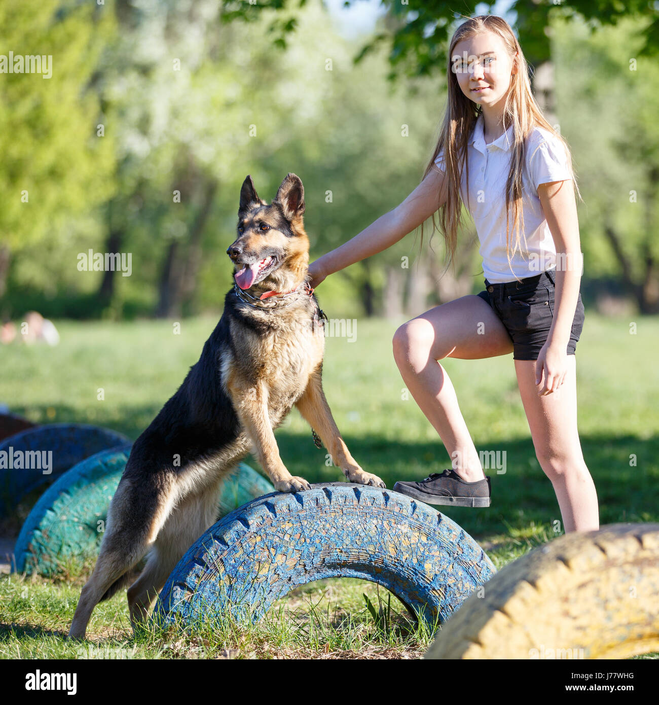 Teenage girl in white shirt with her dog sitting on pathway in the park ...