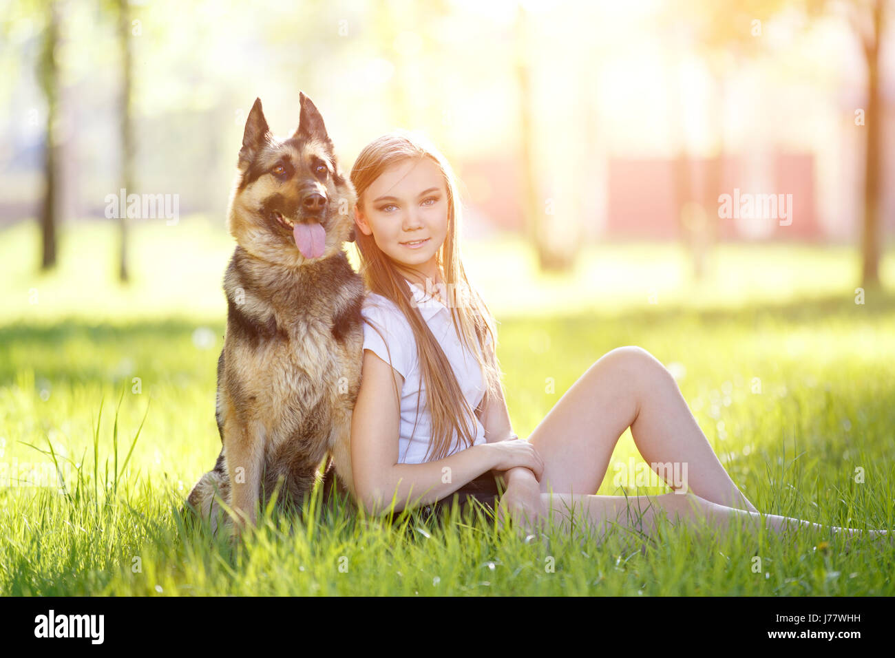 Teenage girl in white shirt with her dog sitting on grass in the park ...