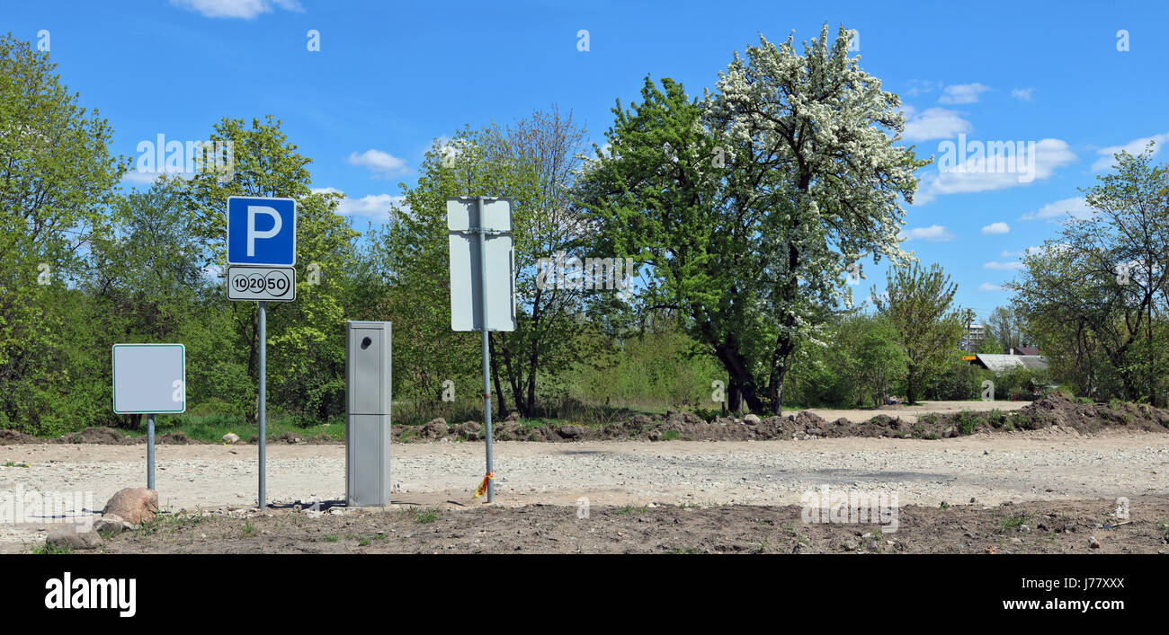 The paid parking is equipped near the village. There is no asphalt, only clay crushed stone and the earth. On a background spring the blossoming apple Stock Photo