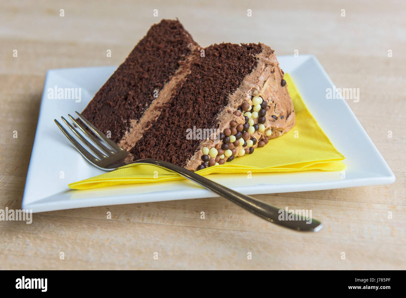 A closeup view of a slice of chocolate cake; Plate; Fork; Serviette; Napkin; Food; Treat; Sweet; Butter icing; Topping; Indulgence; Luxury; Calories Stock Photo