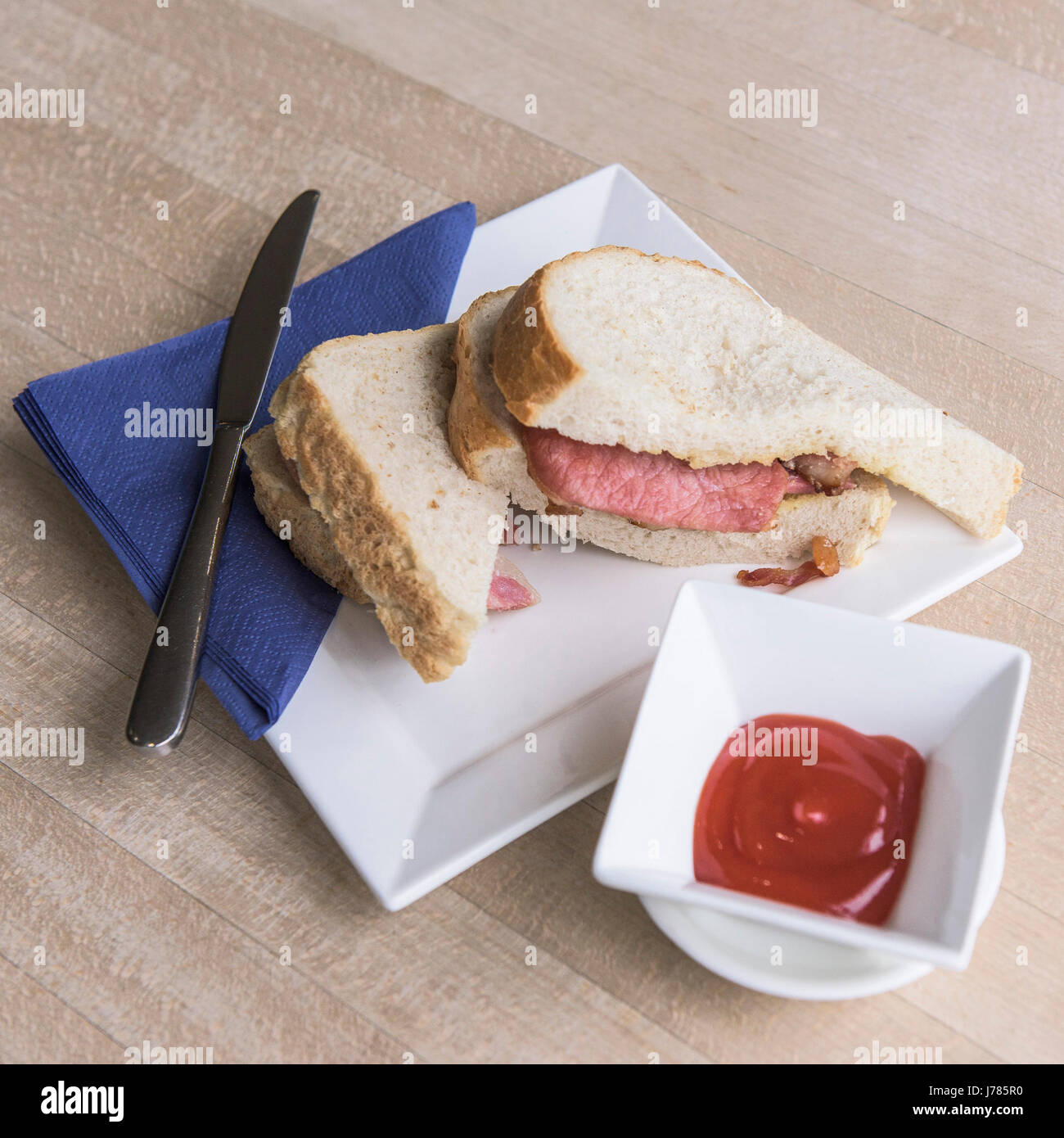 A bacon sandwich; Food; White bread; Bacon rashers; Ketchup; Plate; Knife; Napkin; Stock Photo