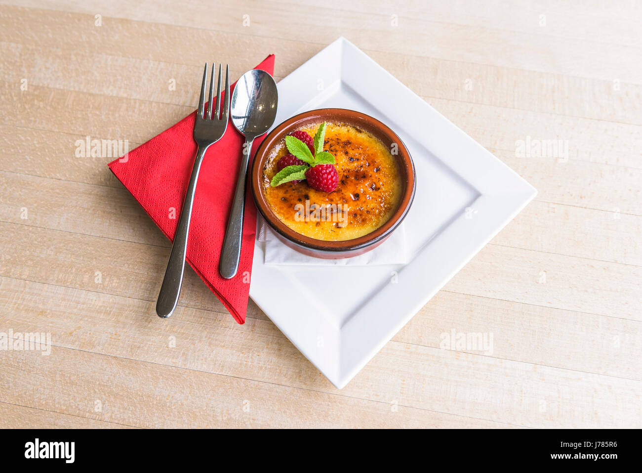 A Creme Brulee served in a restaurant; Dessert; Food; Sweet; Pudding; Cutlery; Rasberries; Tasty; Attractive presentation; Treat; Indulgence; Luxury Stock Photo