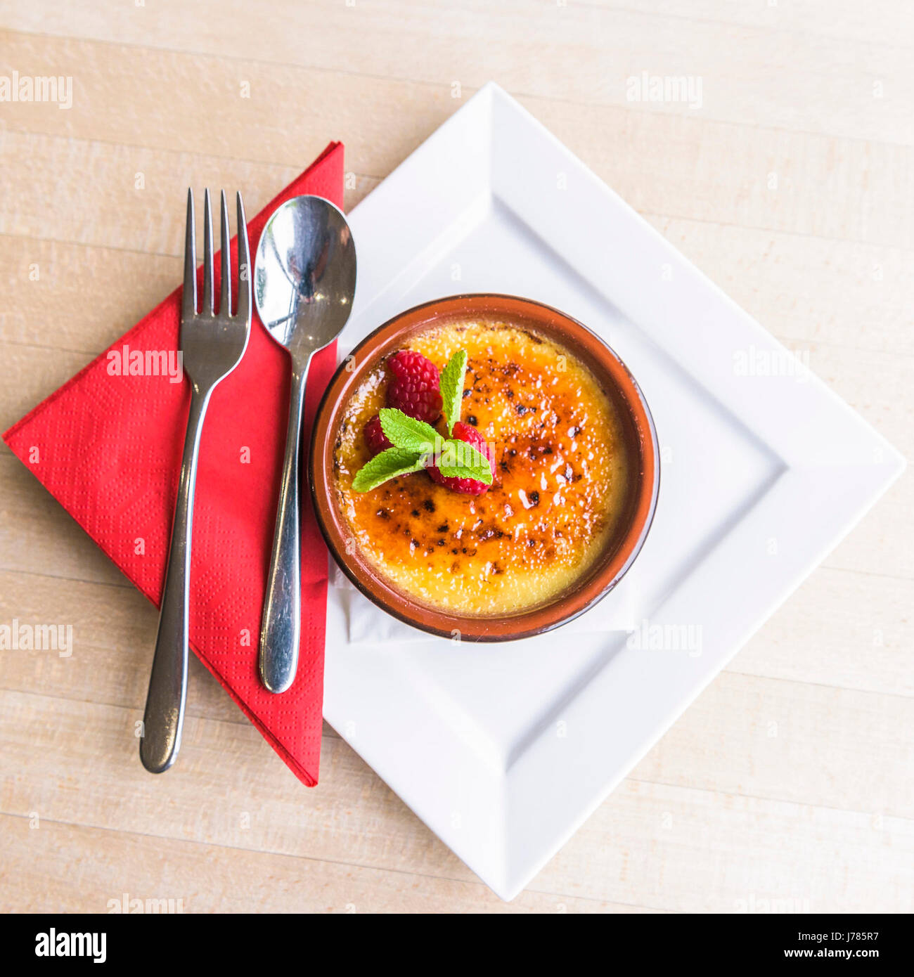 A Creme Brulee served in a restaurant; Dessert; Food; Sweet; Pudding; Cutlery; Rasberries; Tasty; Attractive presentation; Treat; Indulgence; Luxury Stock Photo