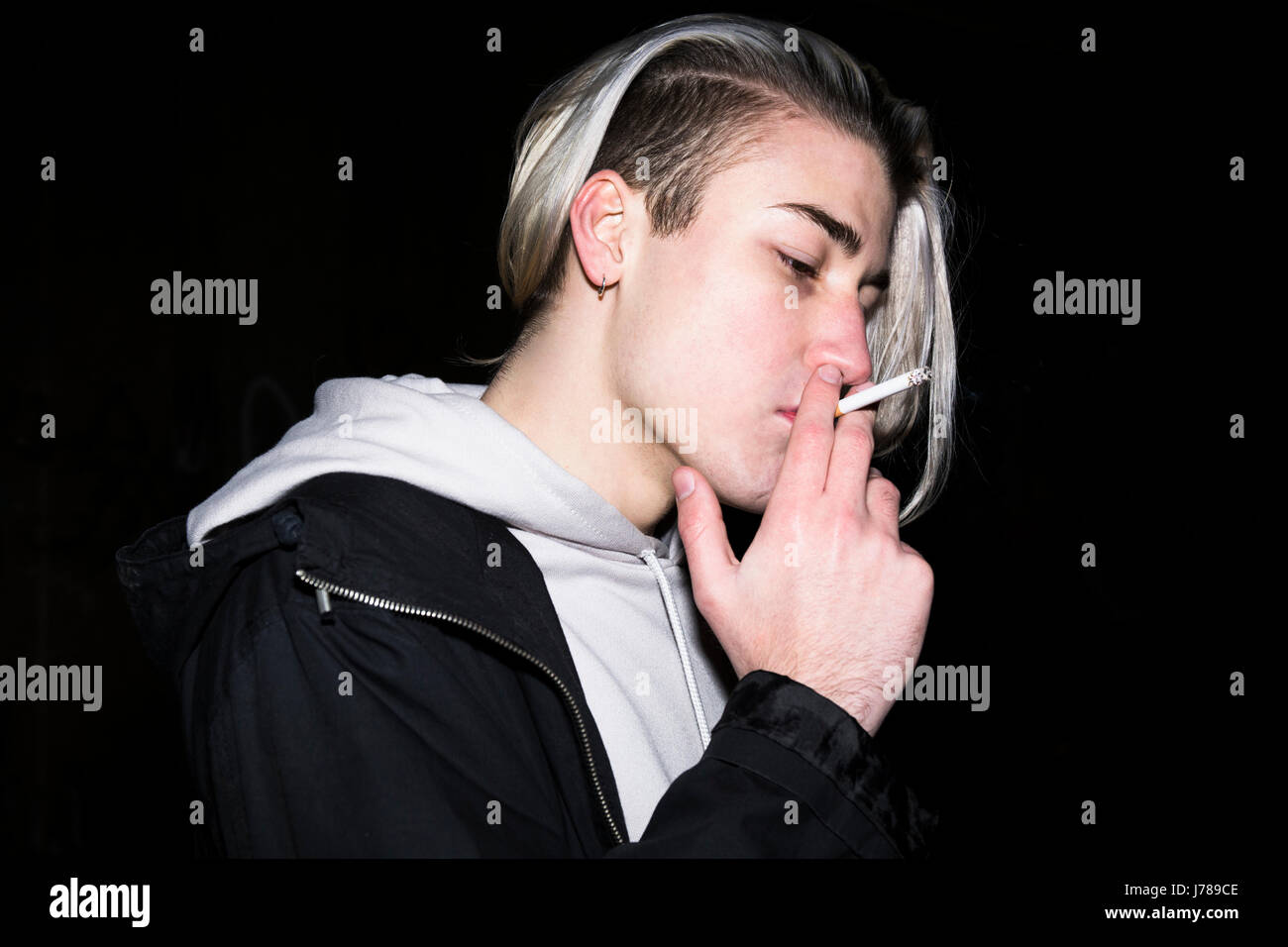 Young man smoking cigarette in front of black background Stock Photo