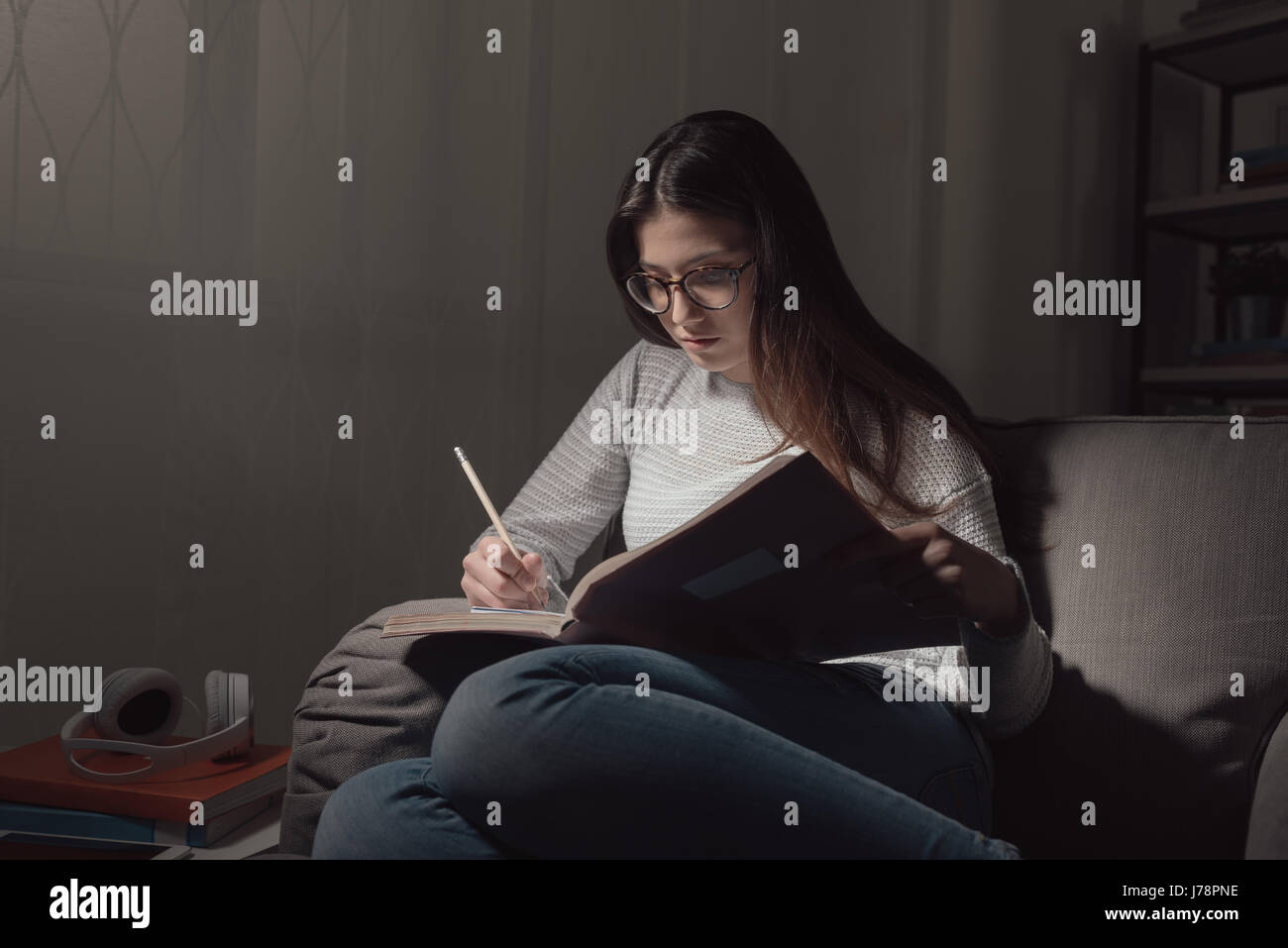 Young woman studying late at night at home, she is sitting on the