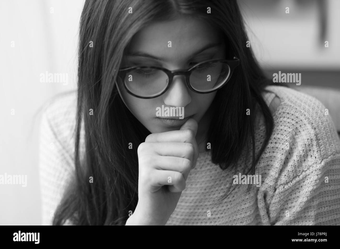 Sad nervous teenage girl with glasses, she is biting nails and looking down Stock Photo