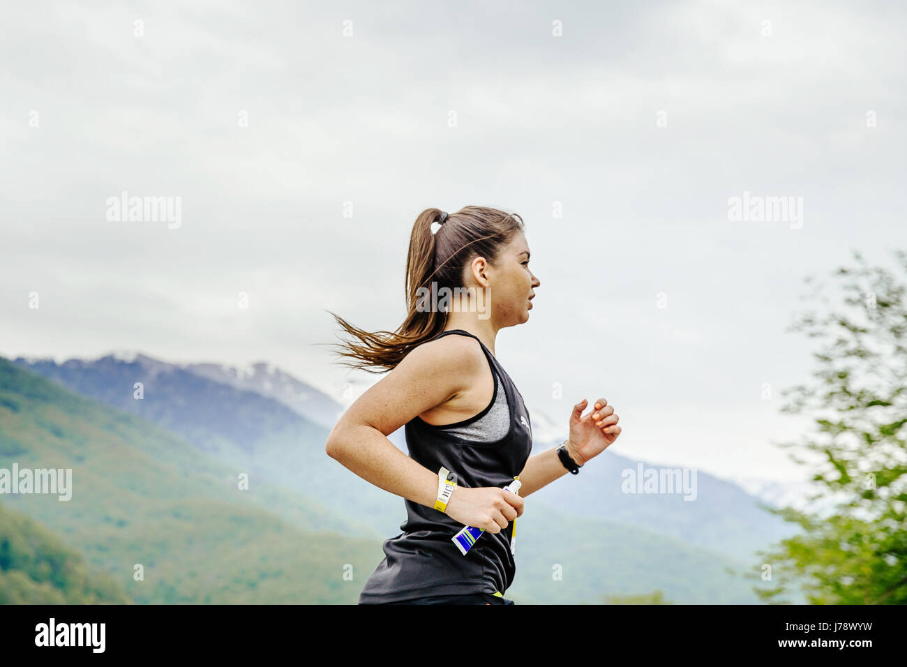young girl runner with energy nutrient gel in hand running in race Spring mountain marathon Stock Photo