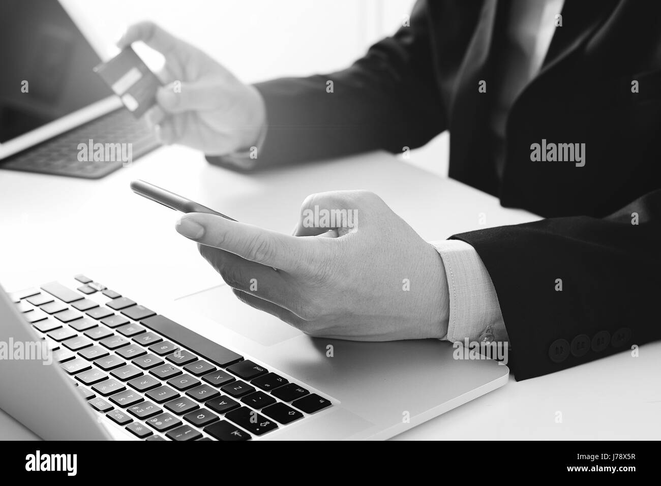 businessman making credit card purchase online with mobile phone and laptop computer on modern desk,black and white Stock Photo