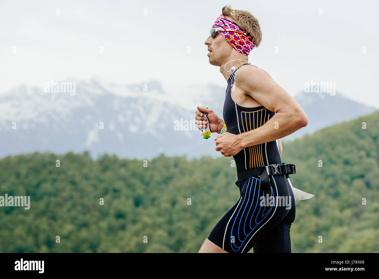 young man runner with energy nutrient gel in hand running in race Spring mountain marathon Stock Photo