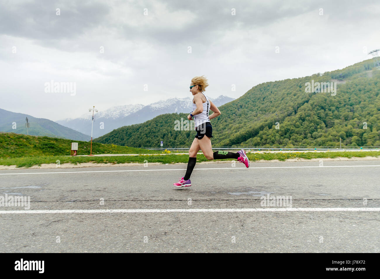 woman runner running in compression socks on asphalt road in race Spring mountain marathon Stock Photo