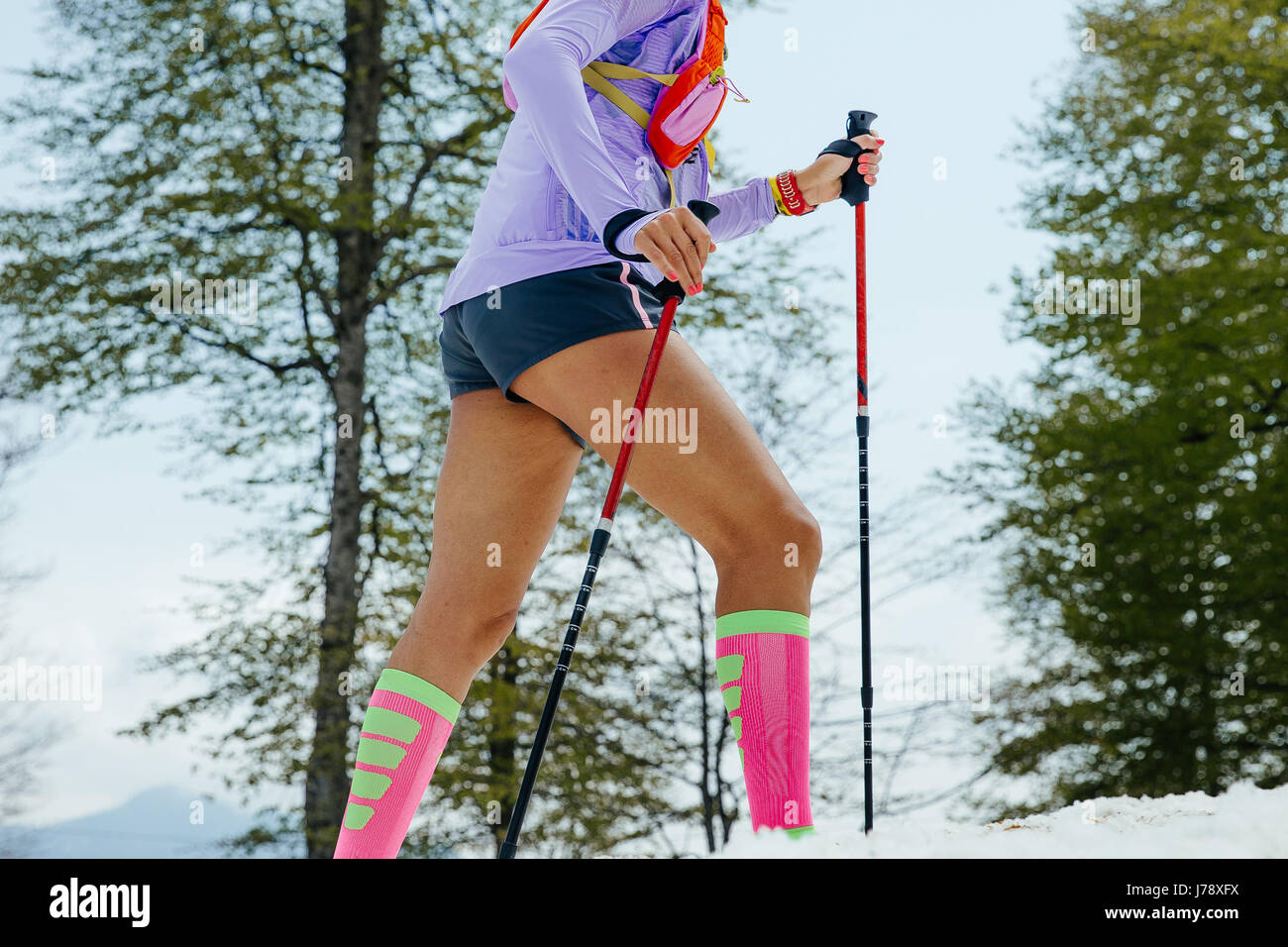female running mountain snowy trail with trekking poles and compression socks Stock Photo