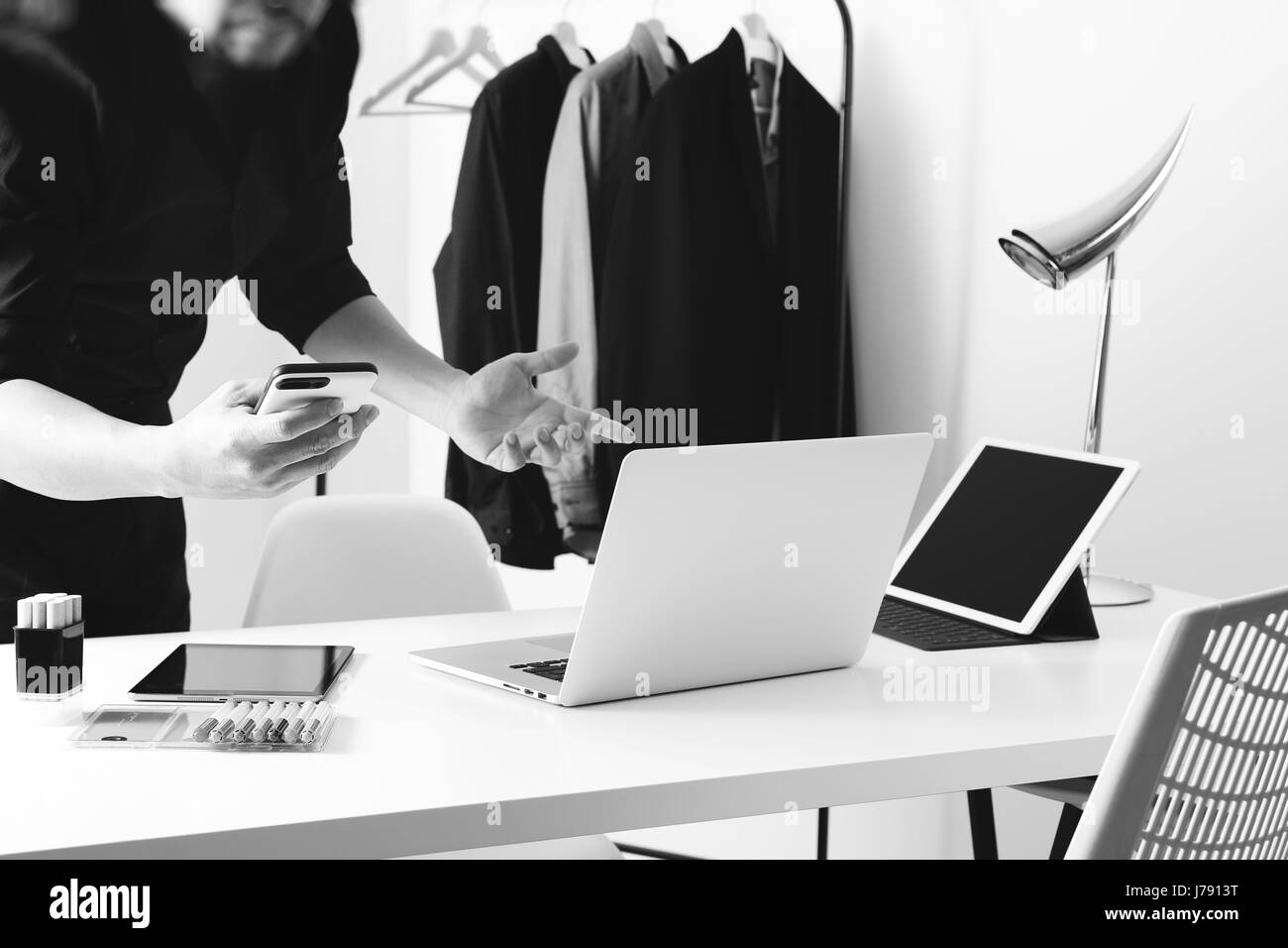 Fashion designer talking mobile phone and using laptop with digital tablet computer in modern studio,black and white Stock Photo