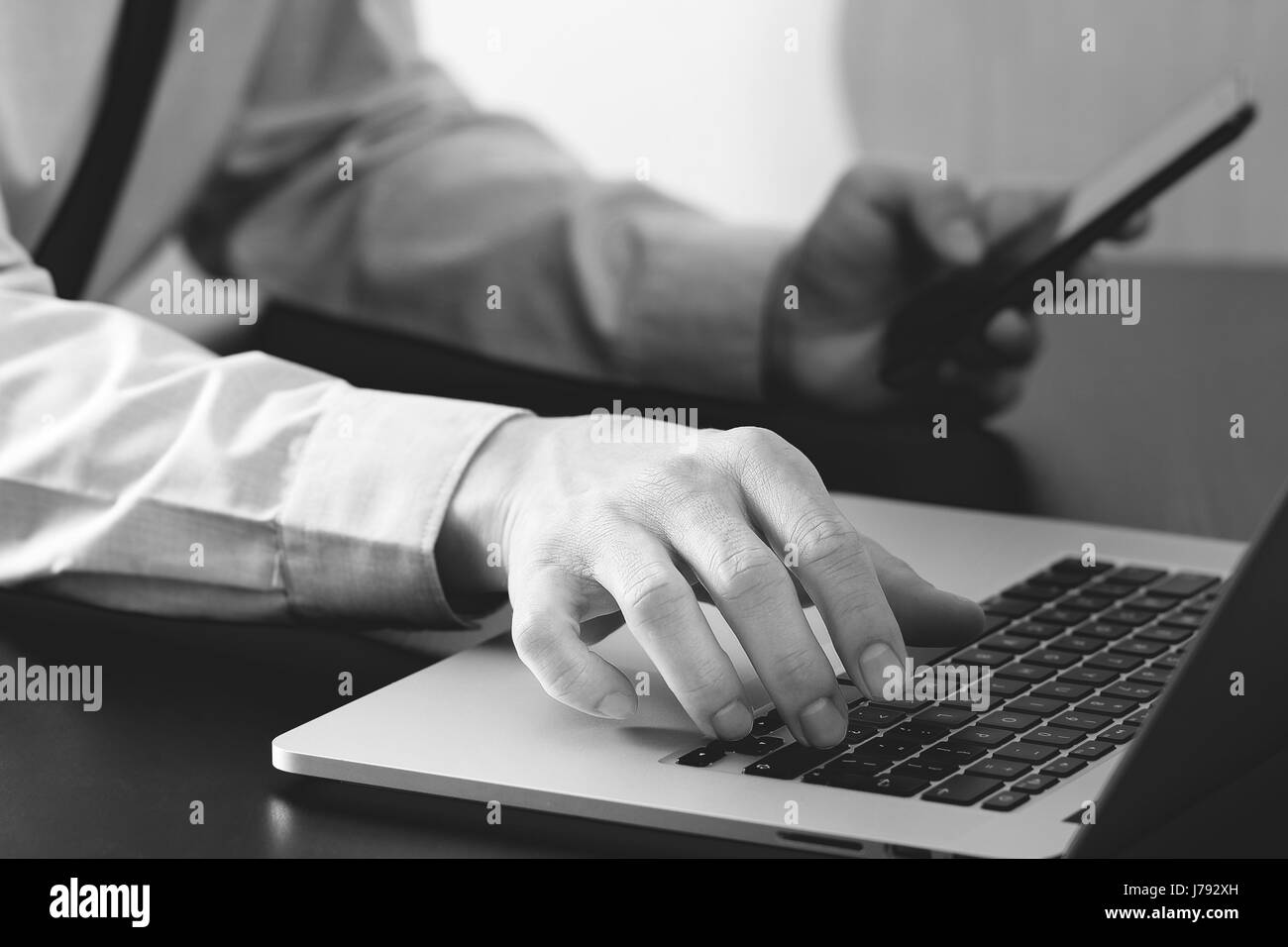 close up of businessman working with mobile phone and laptop computer  on wooden desk in modern office,black and white Stock Photo