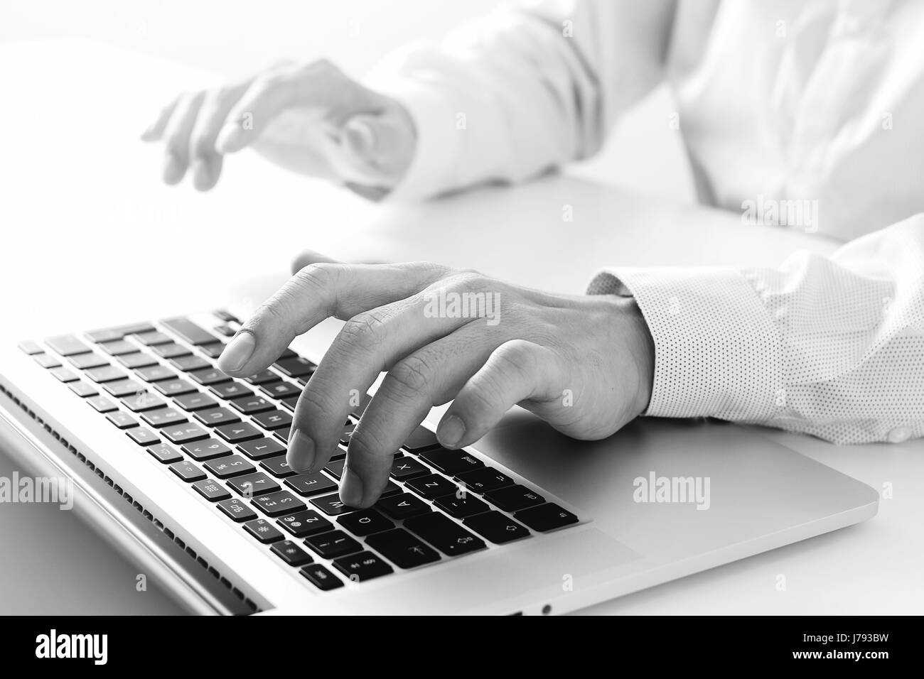 close up of businessman typing keyboard with laptop computer on white desk in modern office,black and white Stock Photo