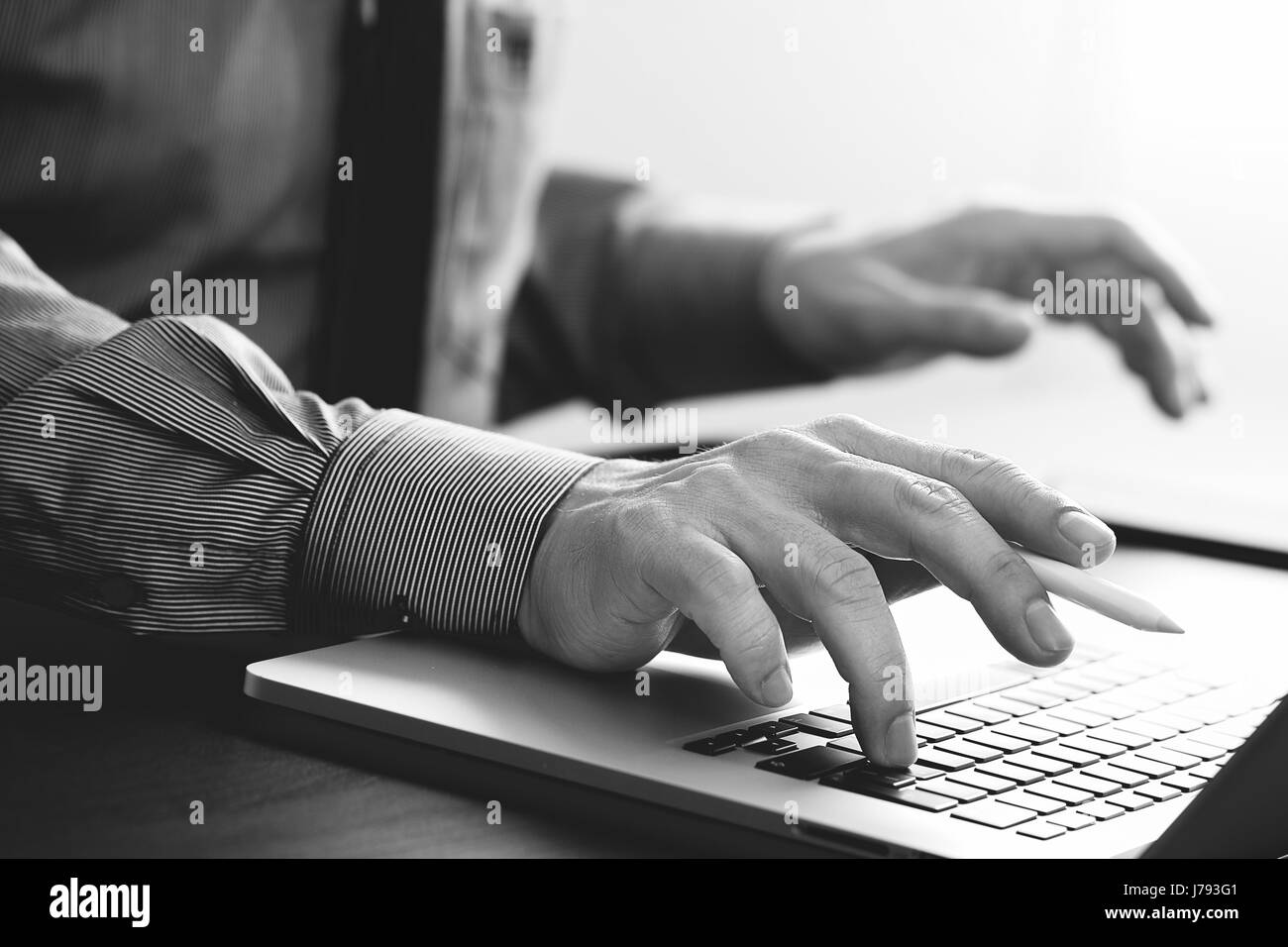 close up of businessman working with mobile phone and stylus pen and laptop computer  on wooden desk in modern office,black and white Stock Photo