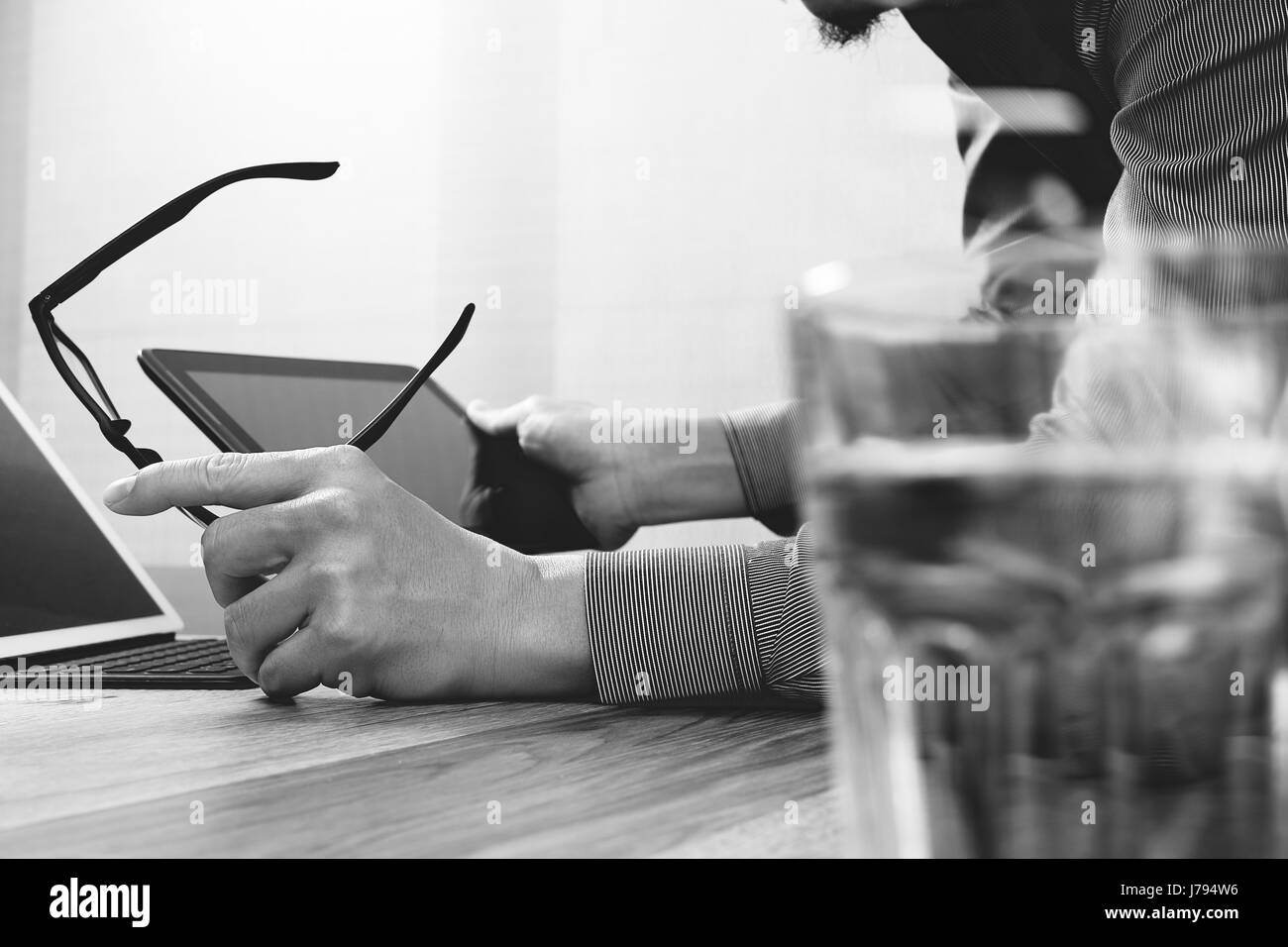 Website designer holding eyeglass working computer laptop,digital tablet on wood table,black white Stock Photo
