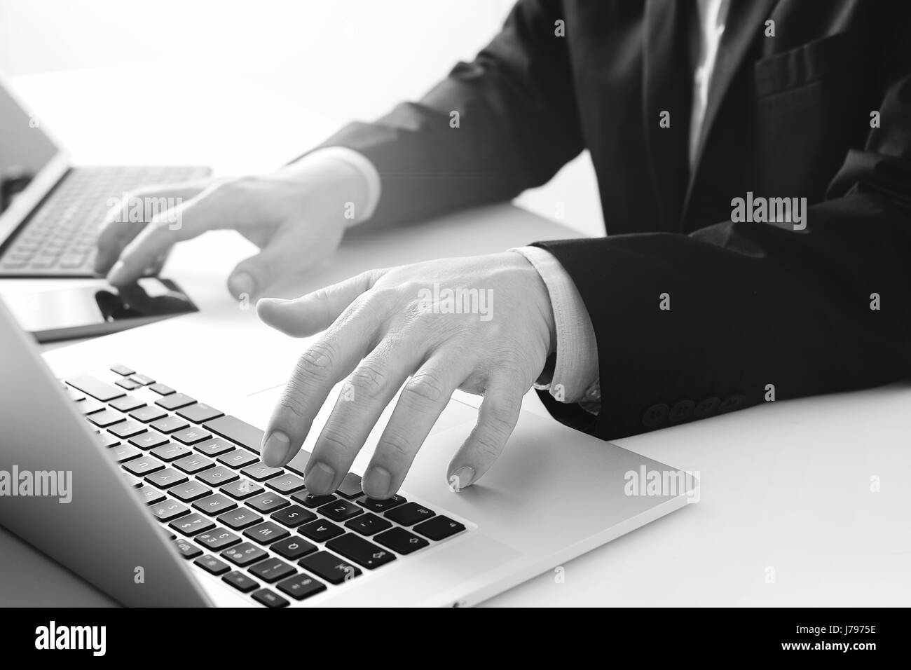 Hands of businessman typing on laptop in modern office with smart phone and digital tablet computer,black and white Stock Photo