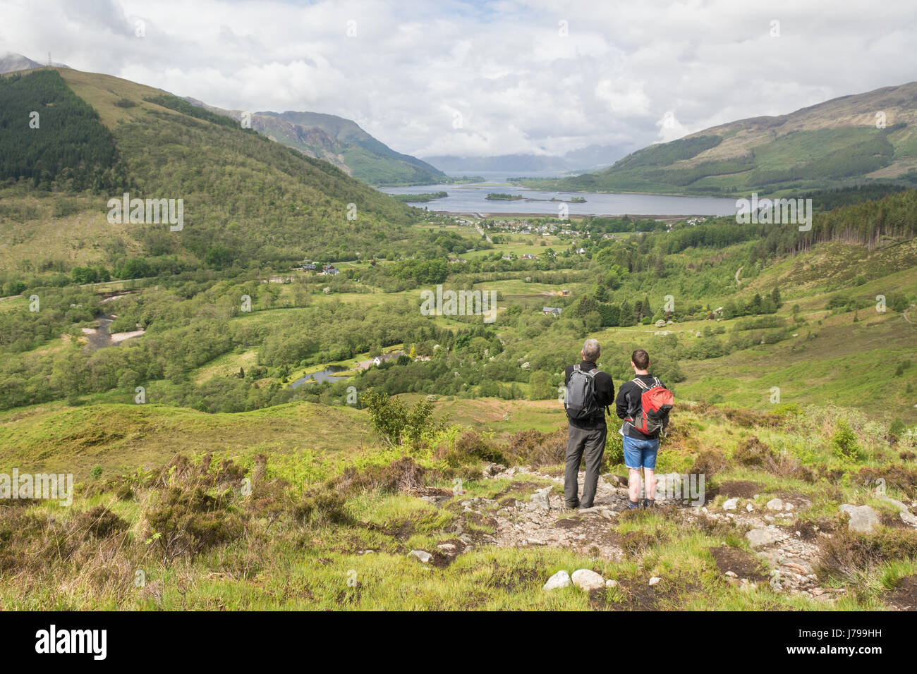 Glencoe village and Loch Leven view - two hikers looking at the view of Glencoe village from the footpath leading up to the Pap of Glencoe, Scotland Stock Photo