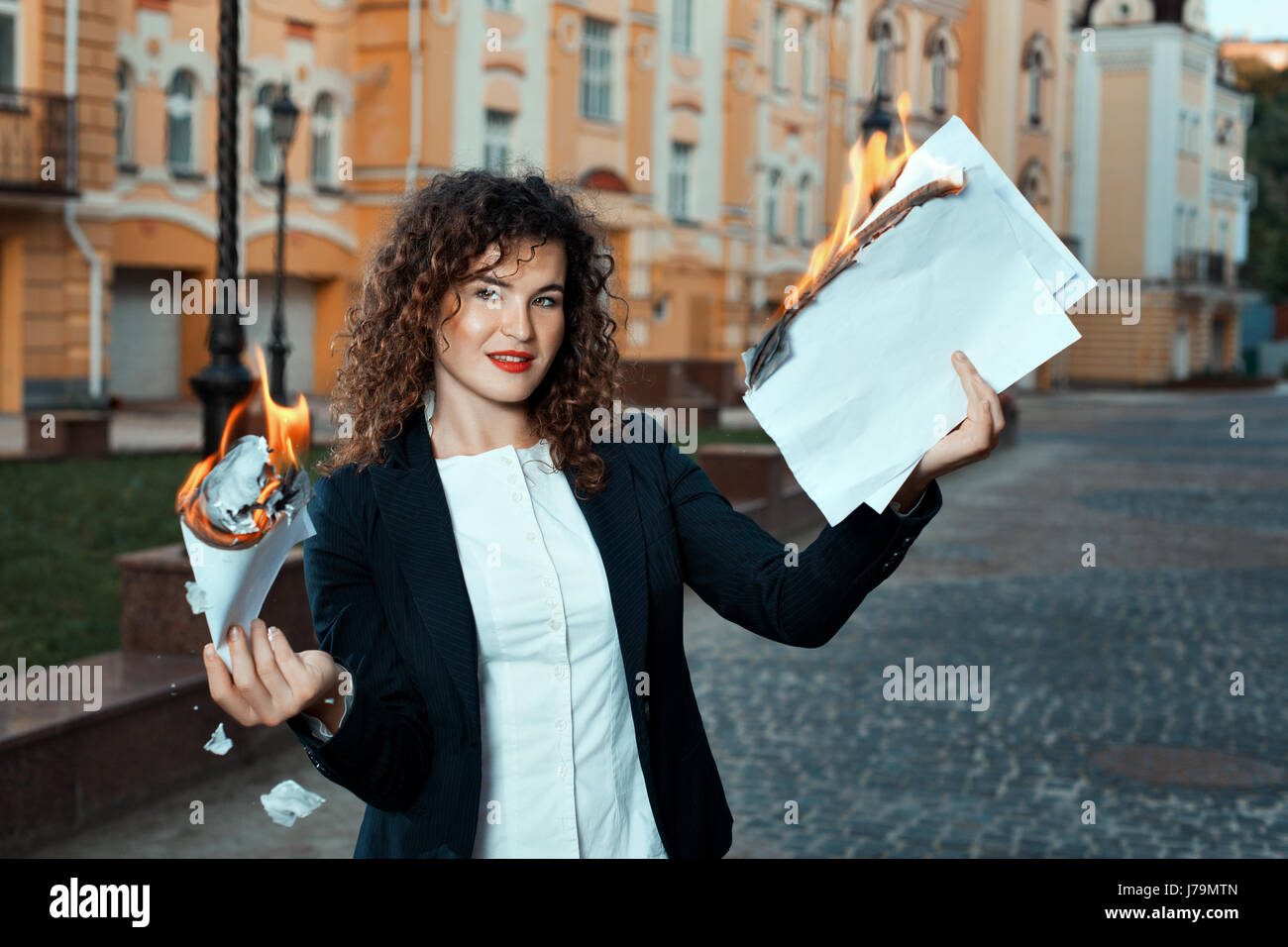 Girl is holding the documents that burn. She is in the city. Stock Photo