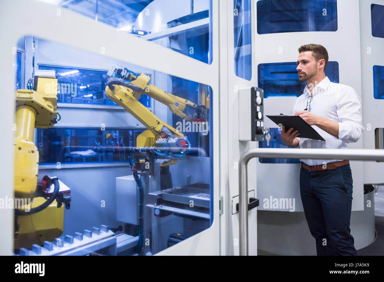 Man taking notes at robotics machine in factory shop floor Stock Photo