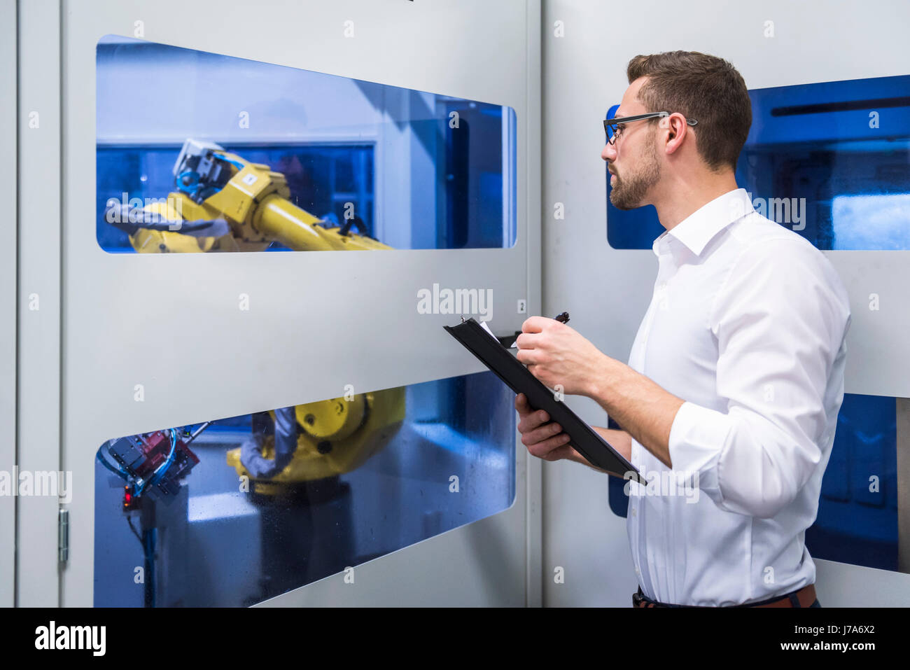 Man taking notes at robotics machine in factory shop floor Stock Photo