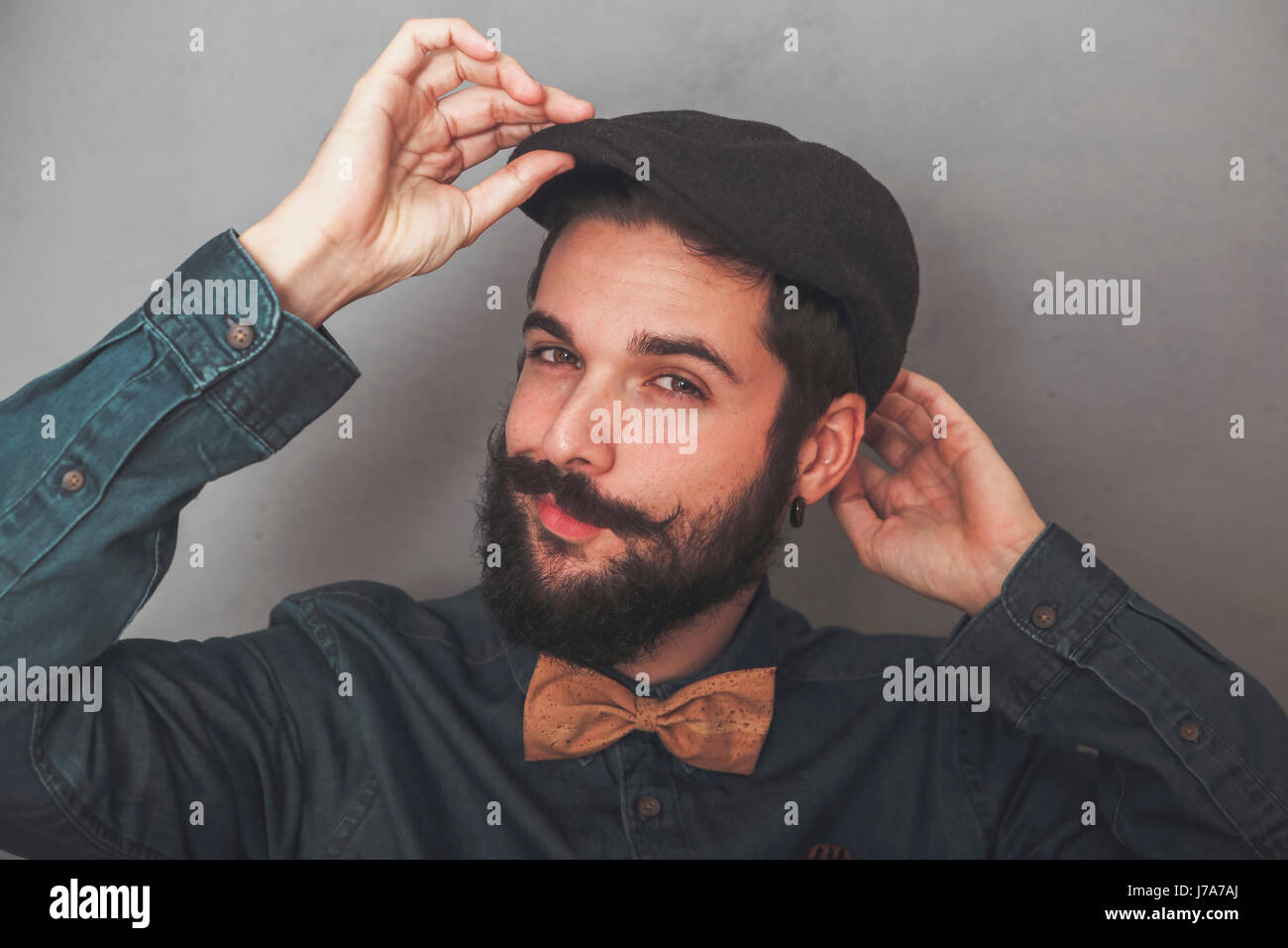 Bearded man putting on his cap, wearing denim shirt and cork bow tie Stock Photo