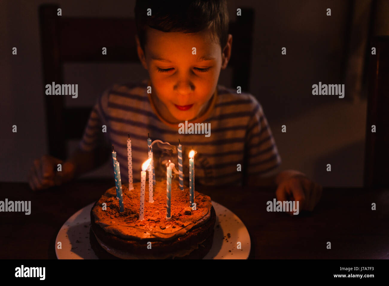 Boy blowing out burning candles on his birthday cake Stock Photo