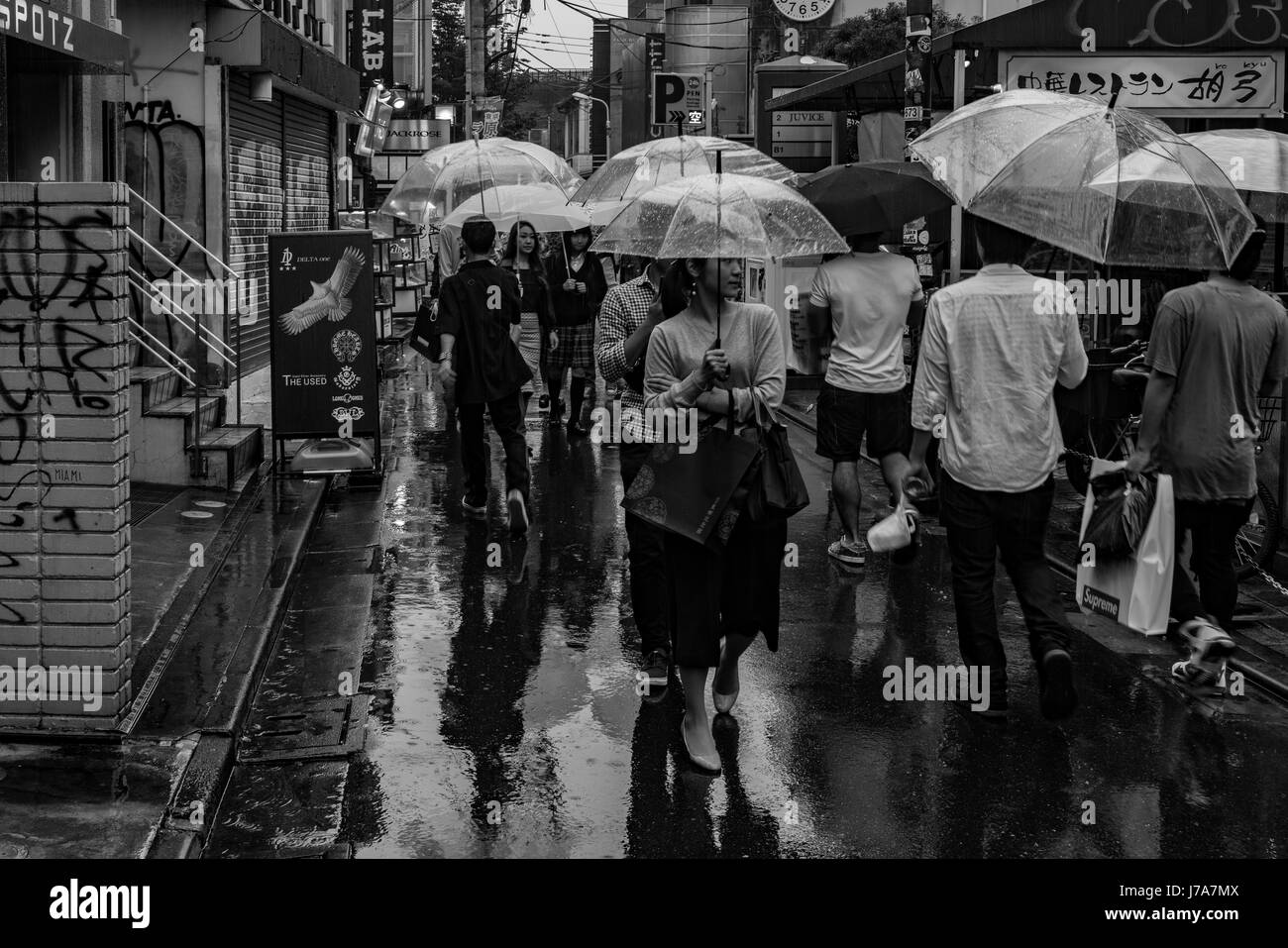 Black and white photo of busy commercial area with people waking up and down the wet street. Stock Photo