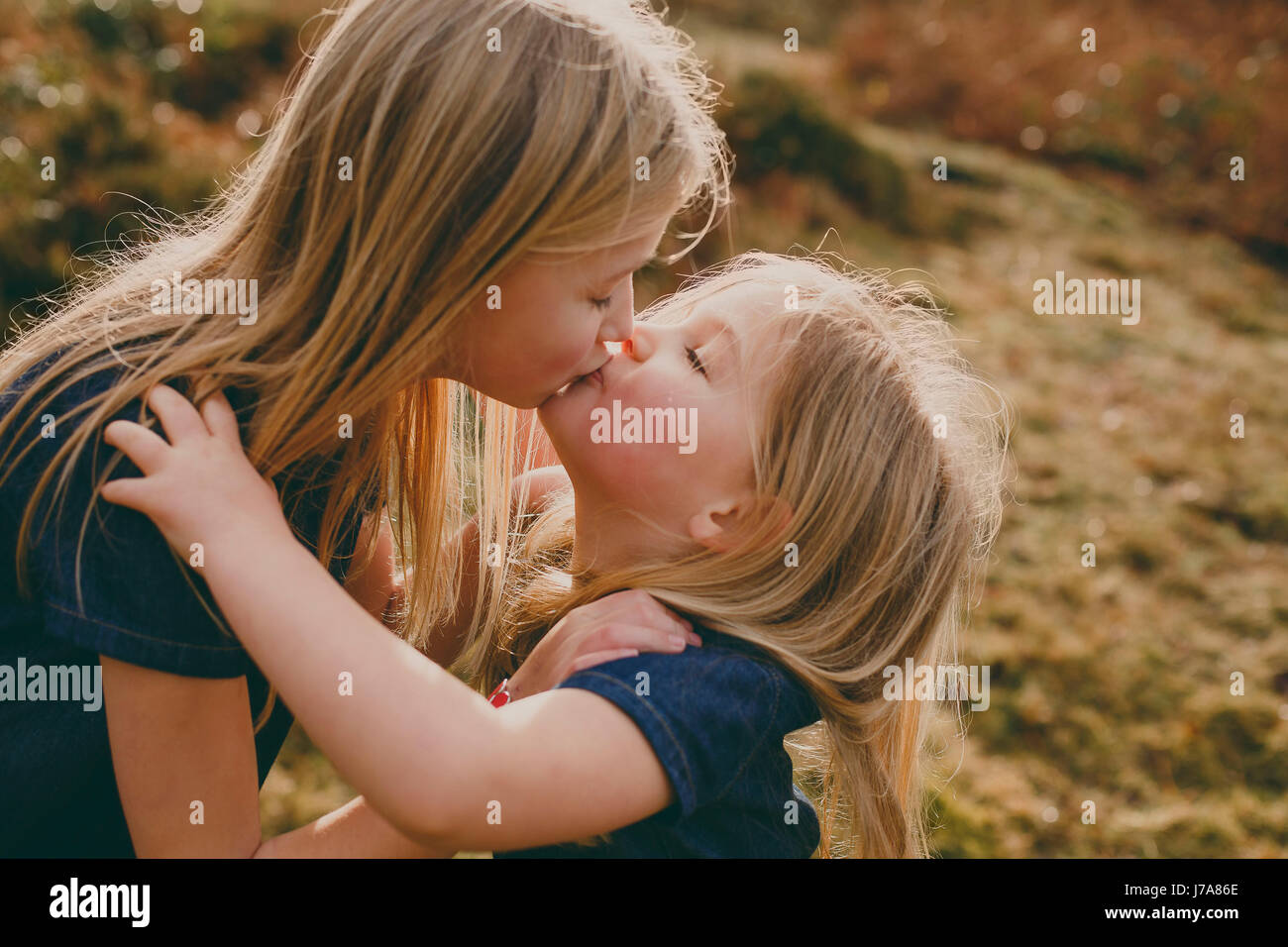 Two cute blond sisters kissing outdoors Stock Photo