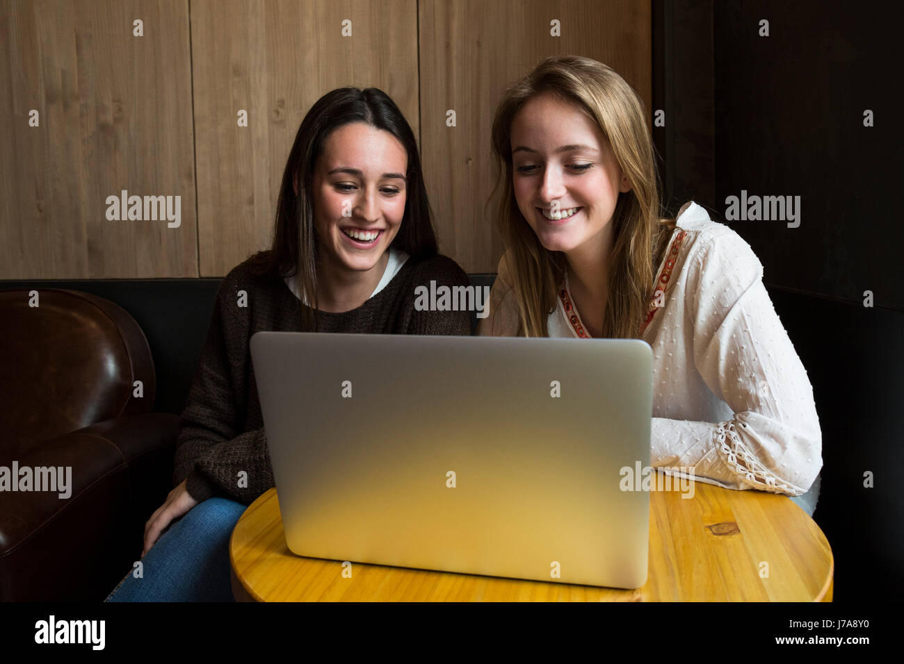 Two smiling friends sitting in a coffee shop looking at laptop Stock Photo
