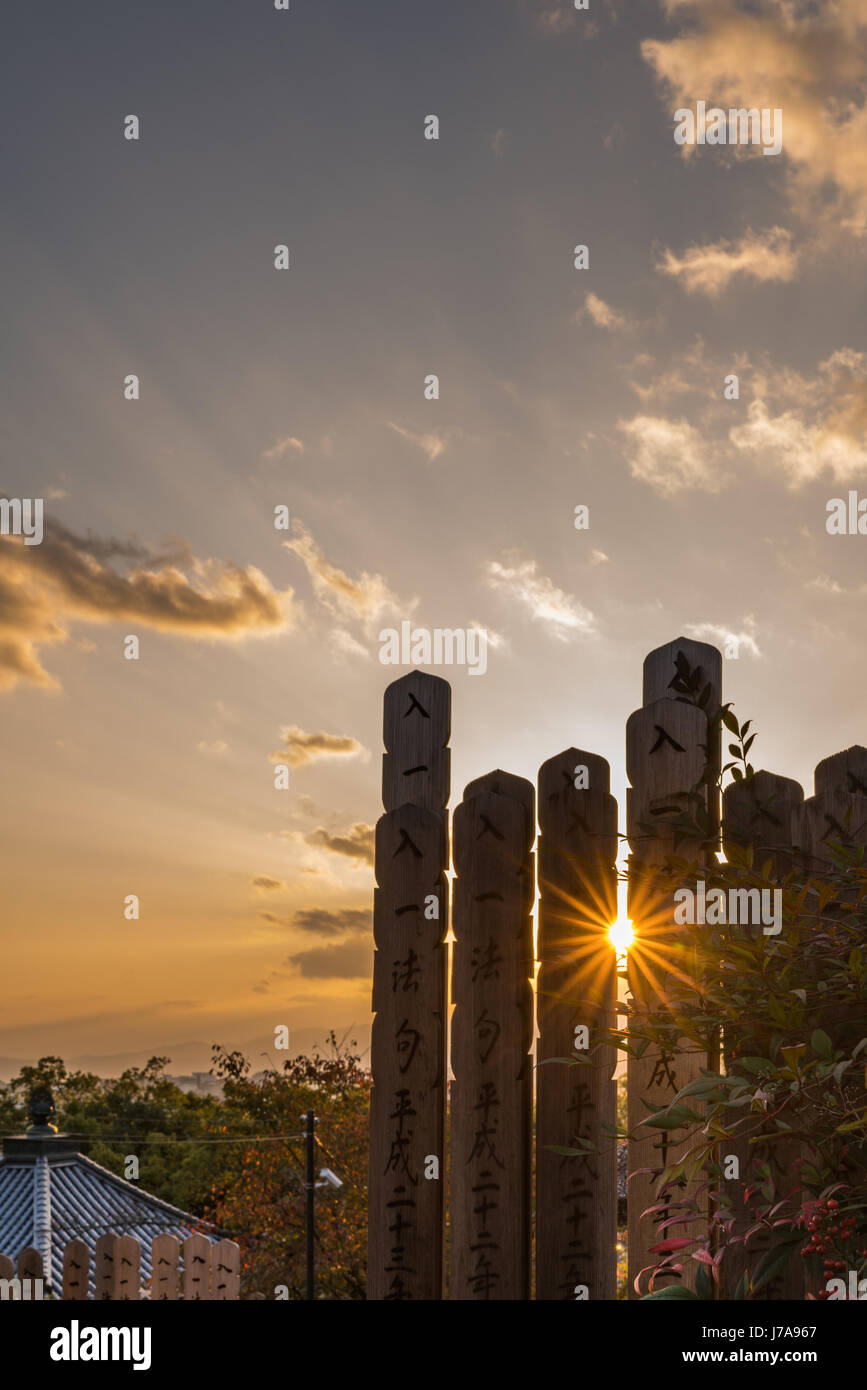 Beautiful sunset captured between two of several tall columns with Japanese characters written on them. The golden sun star effect is magical. Stock Photo