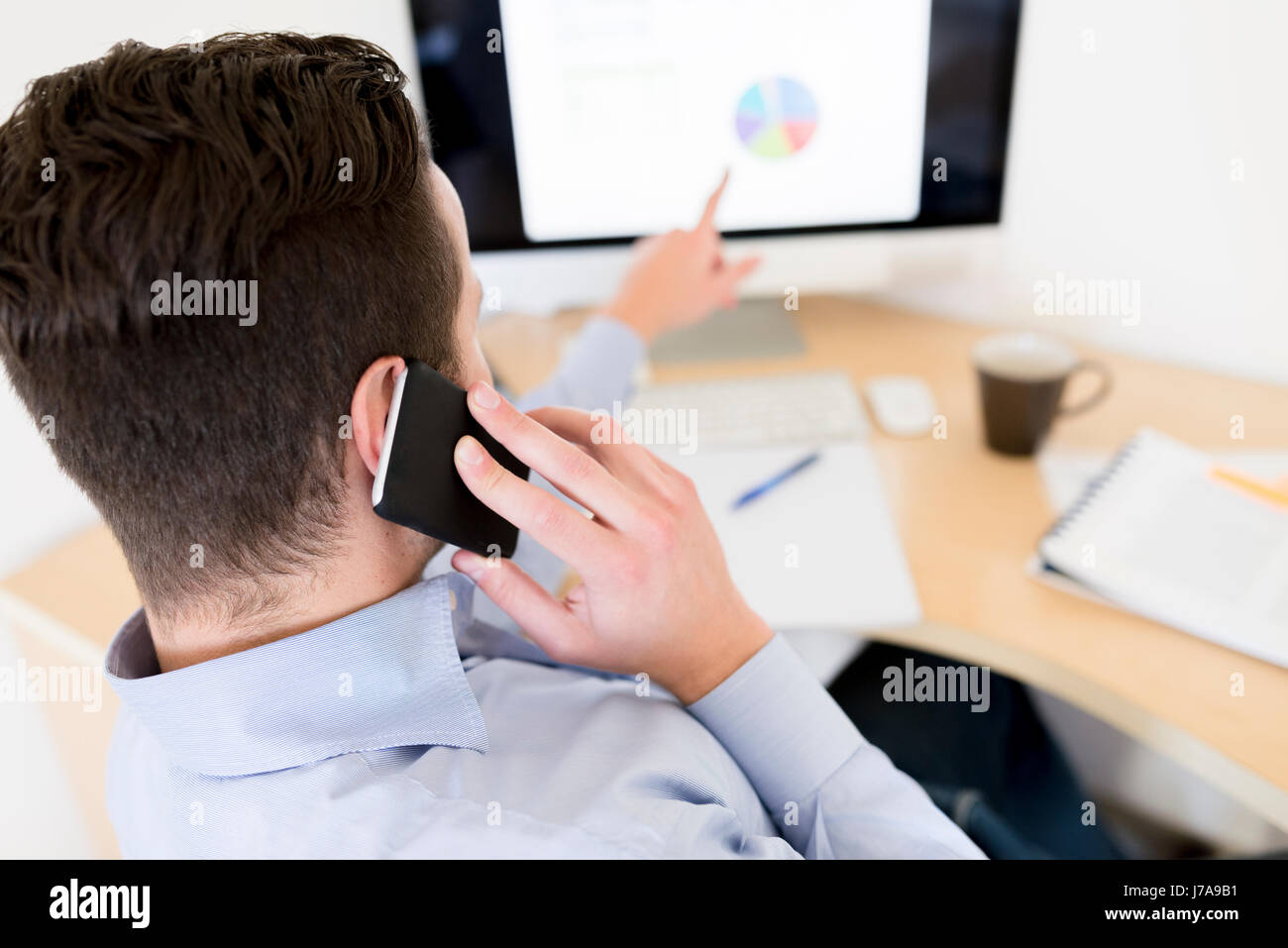 Businessman on the phone analysing pie chart on computer screen Stock Photo