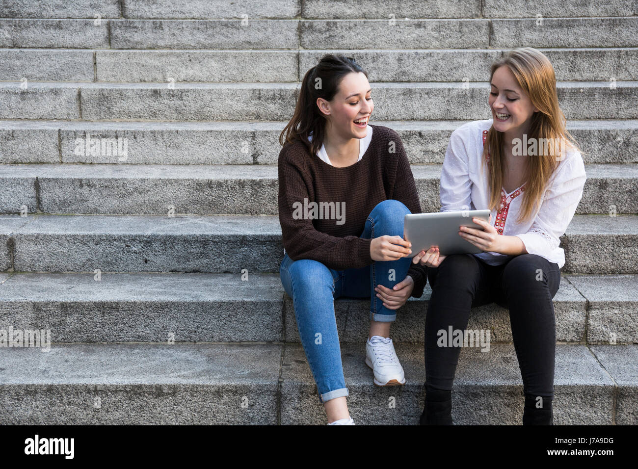 Two friends sitting on stairs using cell phone Stock Photo