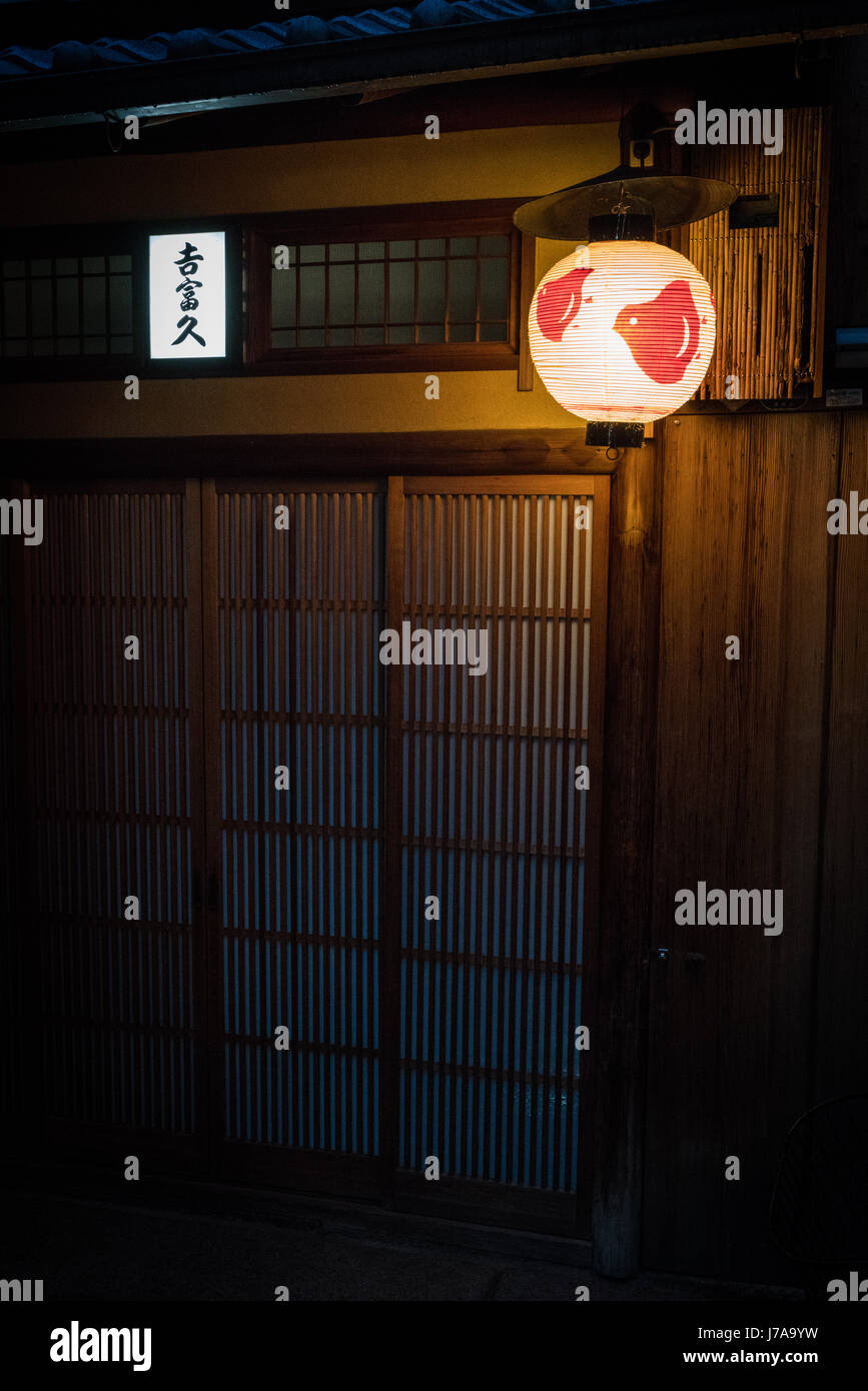 Thin wooden strips cover the facade of this building, allowing light to pass through it . A round, white and red paper lantern hangs above the door. Stock Photo