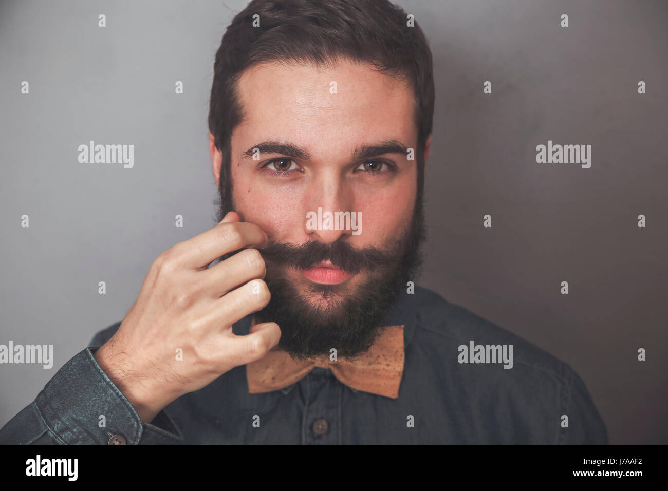 Bearded man adjusting his moustache, wearing denim shirt and cork bow tie Stock Photo