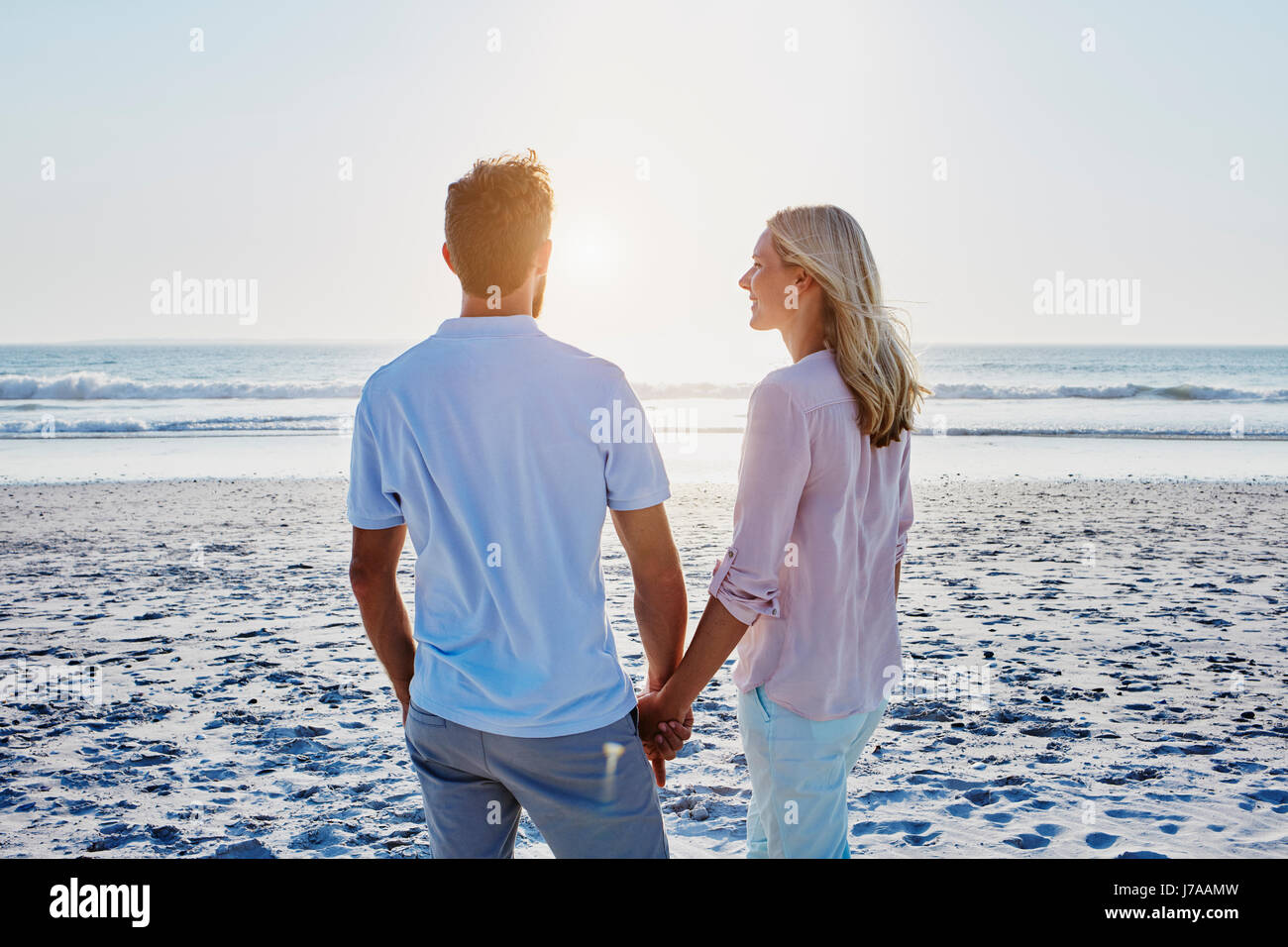 Couple holding hands on the beach at sunset Stock Photo - Alamy