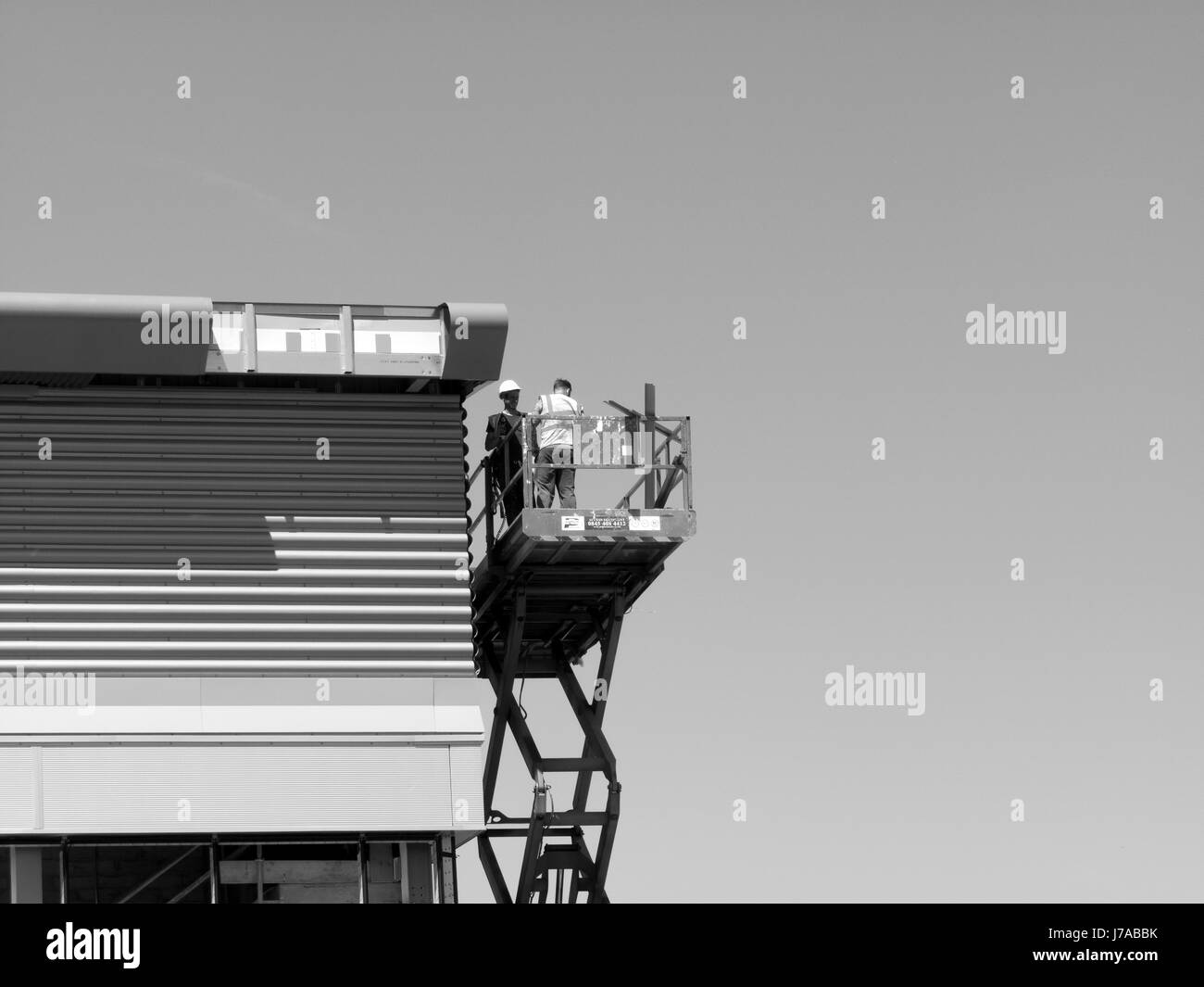 construction workers on mobile scissor lift installing cladding to new commercial warehouse development Stock Photo