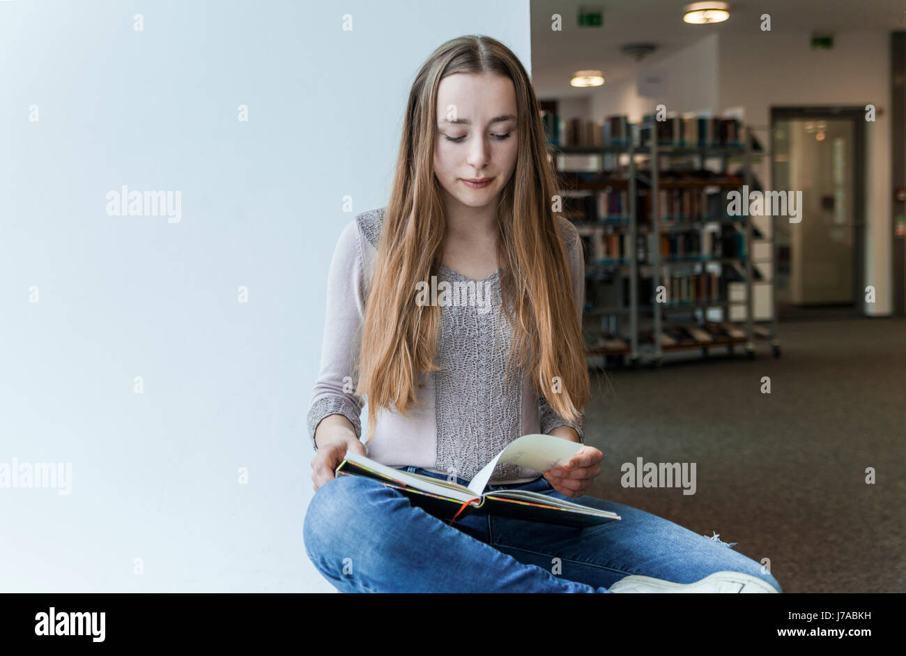 Teenage girl reading book in a public library Stock Photo - Alamy