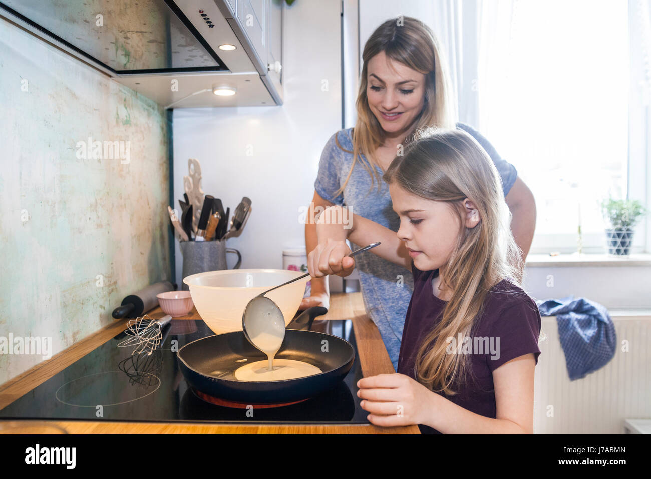 Mother and daughter baking pancakes in kitchen Stock Photo