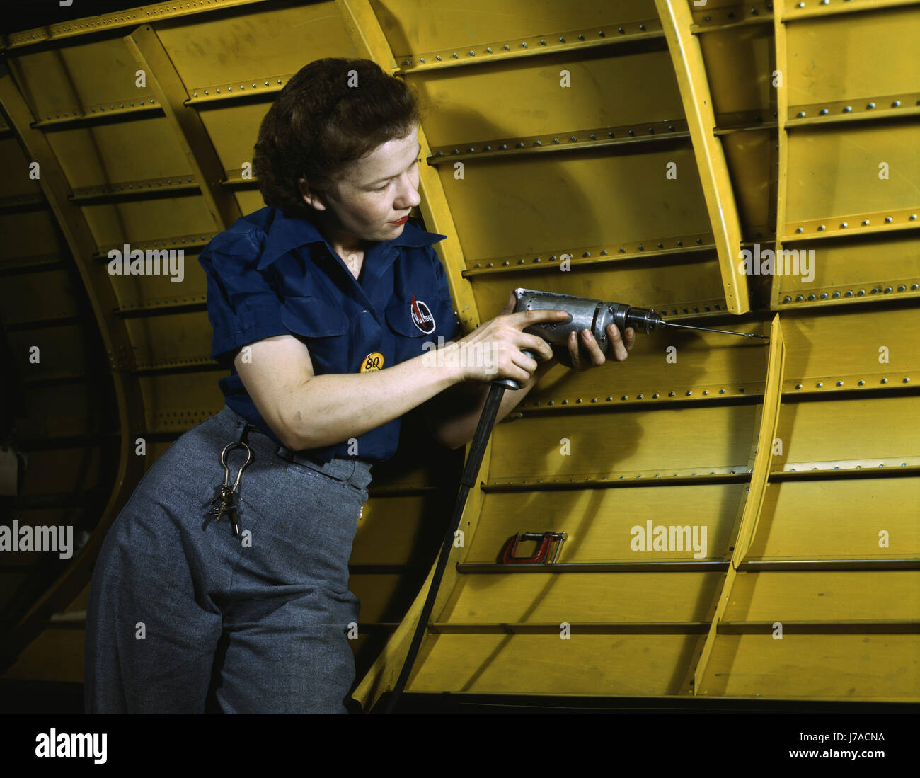 Woman operating a hand drill while working on an A-31 Vengeance dive bomber, 1943. Stock Photo