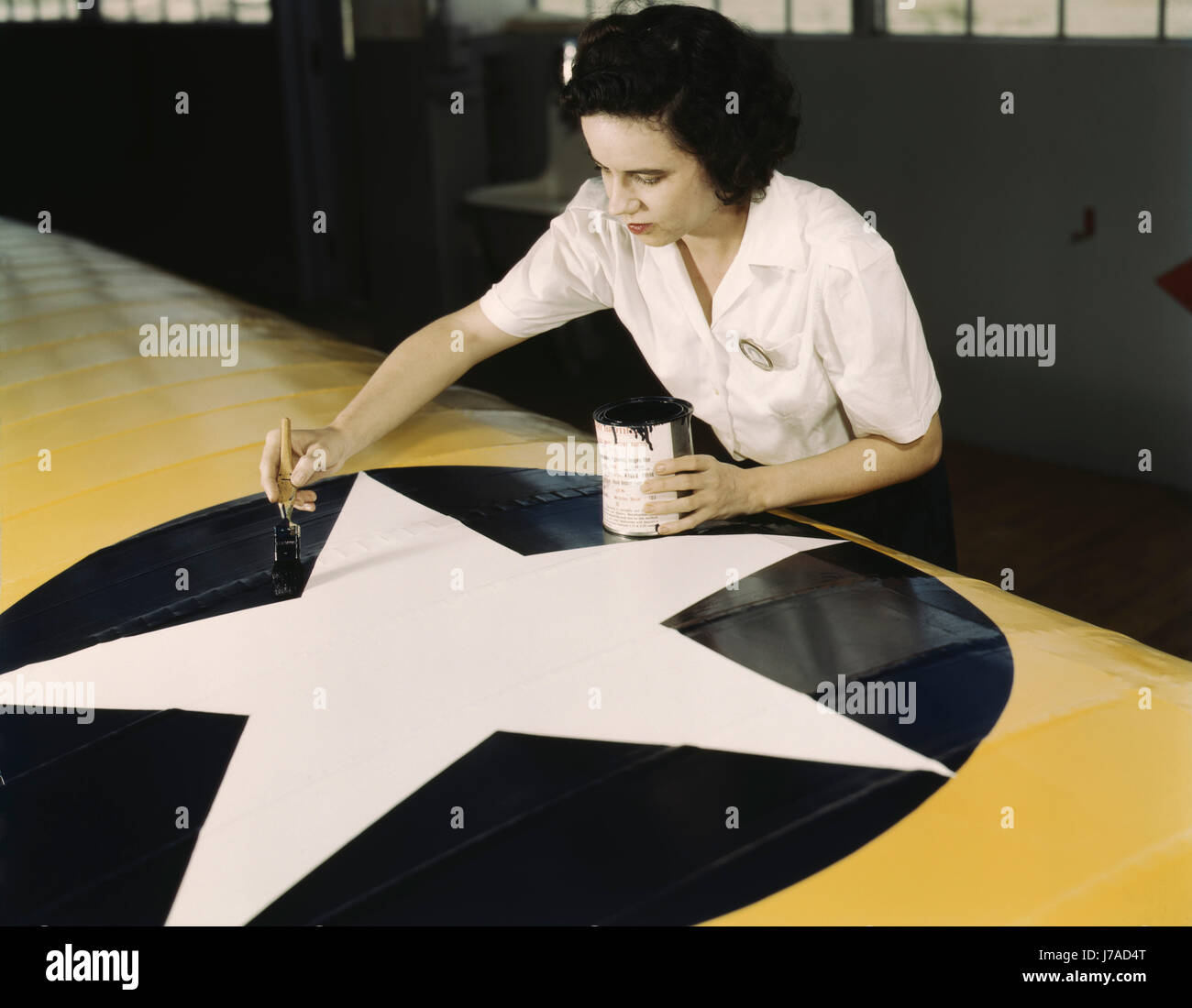 A female worker paints the American insignia on a Navy plane wing, 1942. Stock Photo