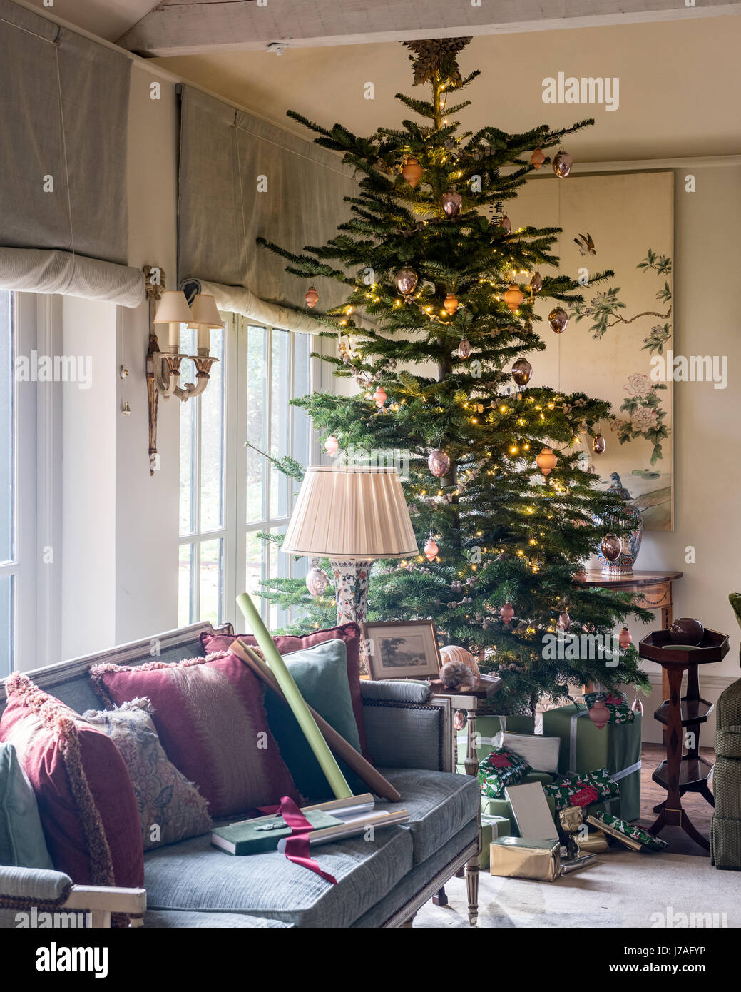 Tall christmas tree in corner of spacious sitting room with settee and old chinese painted panels. The sofa upholstery and blinds are from Colefax and Stock Photo