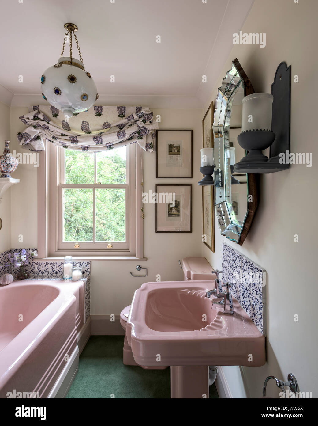 Pink enamelled cast iron bath and basin in bathroom with Fired Earth tiles and ornate gilt mirror Stock Photo