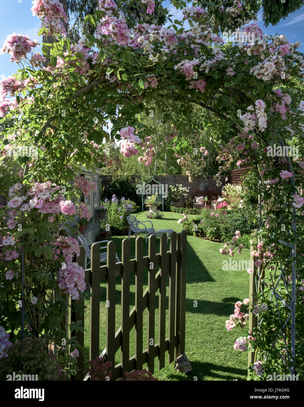 Picket gate underneath rose arch leading through to charming english walled garden Stock Photo