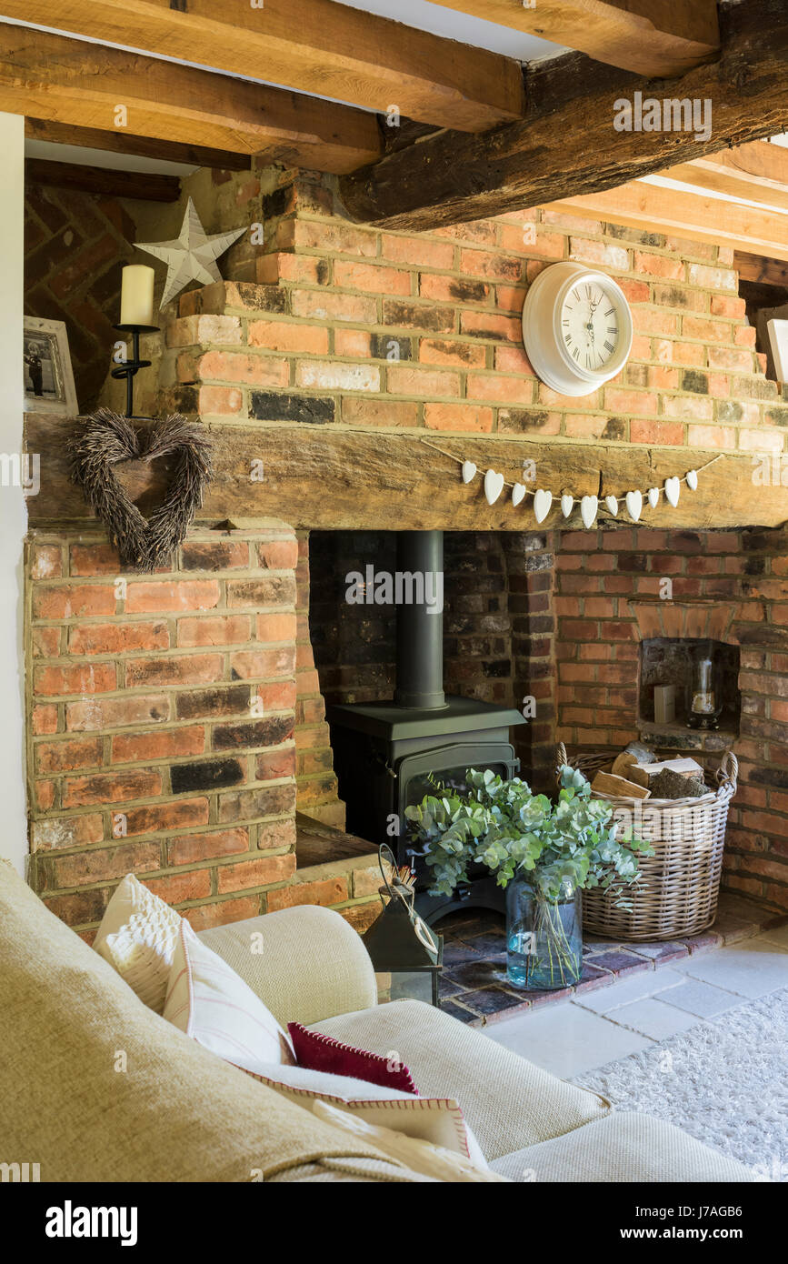 Cosy sitting room with inglenook fireplace, exposed brick wall and wood beamed ceiling. The cream sofa is from Laura Ashley and the rug from John Lewi Stock Photo