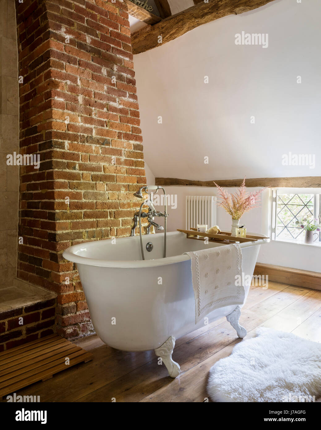 Vaulted bathroom with ancient beams, exposed brick wall and roll-top French bath. Stock Photo