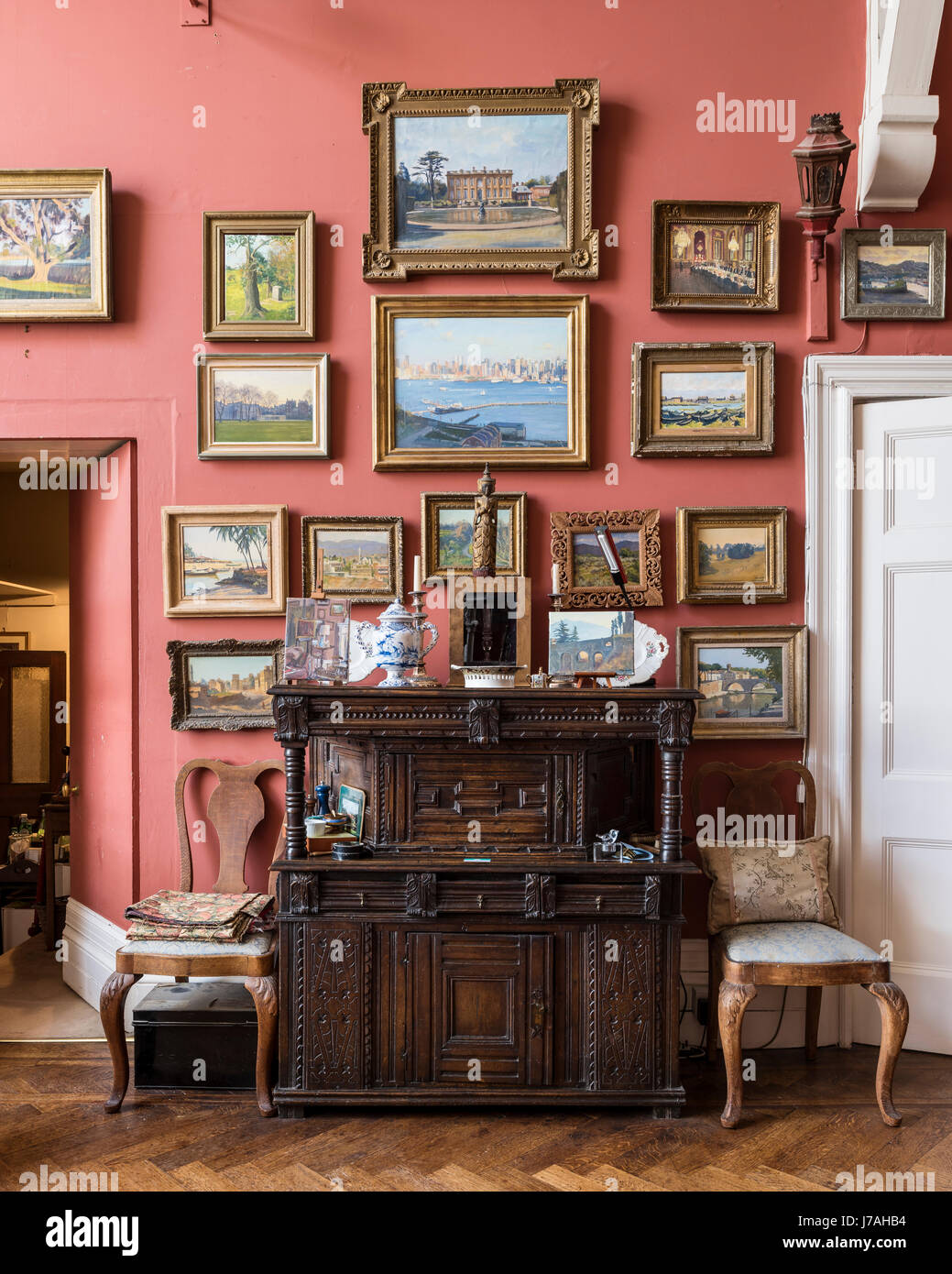 A collection of Julian Barrow paintings above a Tudor-style press. the  walls are painted in Farrow & Ball's Book Room Red Stock Photo - Alamy