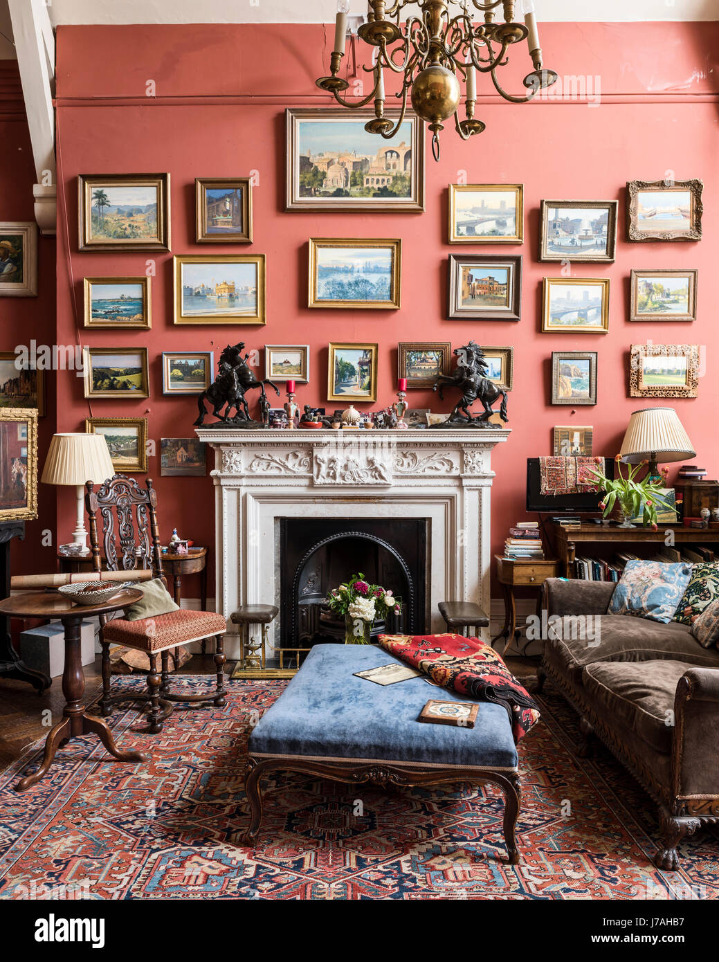 A collection of Julian Barrow paintings above a salvaged chimney piece. Clustered around are a Victorian bergere sofa and a Charles II style chair. Th Stock Photo