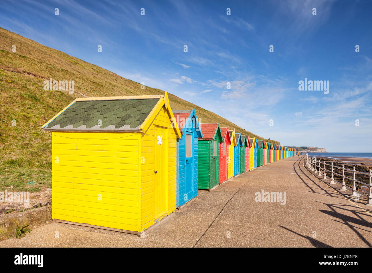 Colourful beach huts lining the promenade at North Beach, Whitby, North Yorkshire, England, UK, early on a bright sunny spring morning. Stock Photo